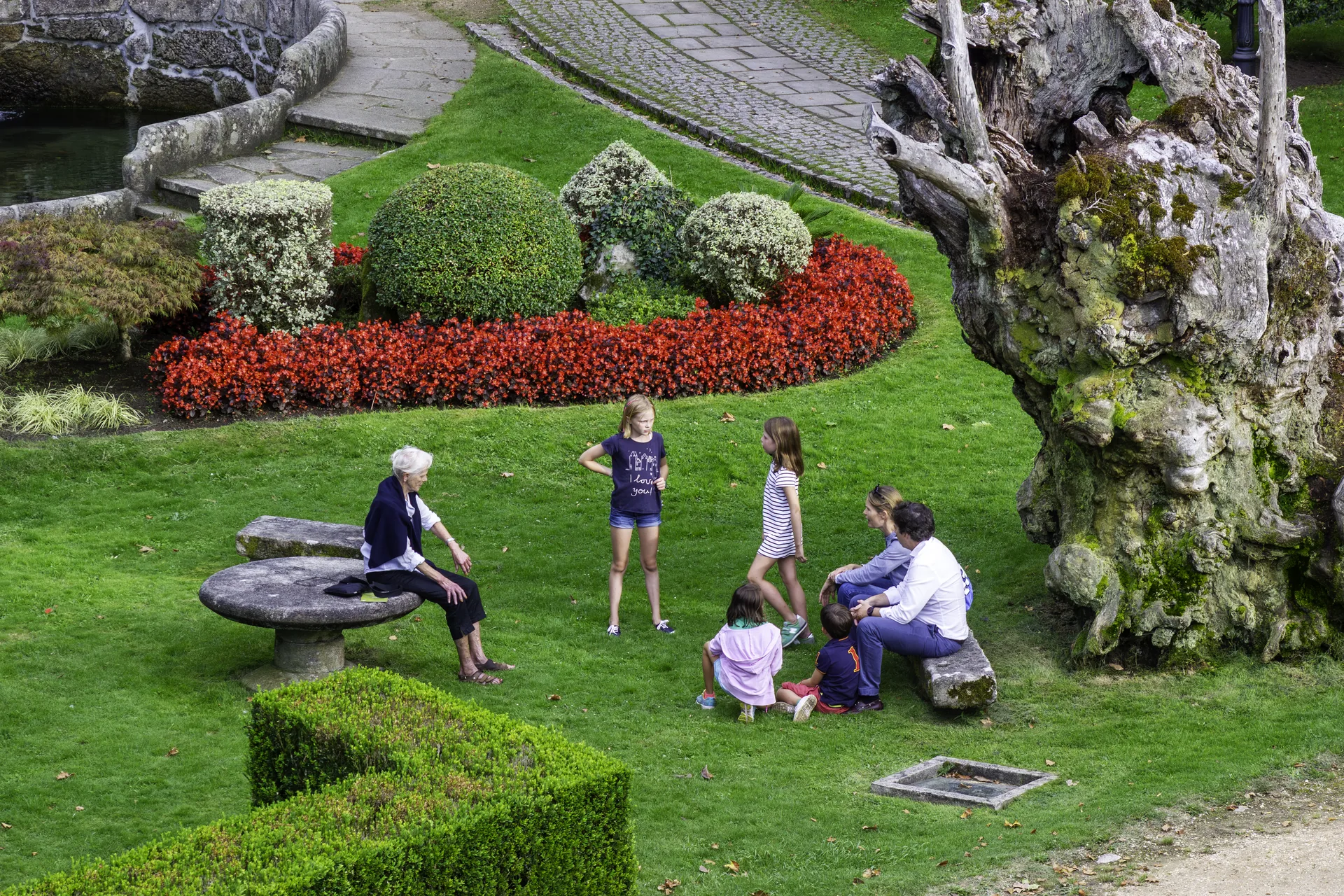 Visitantes percorrem o jardim histórico do Castelo de Soutomaior, cercado por árvores e vegetação.