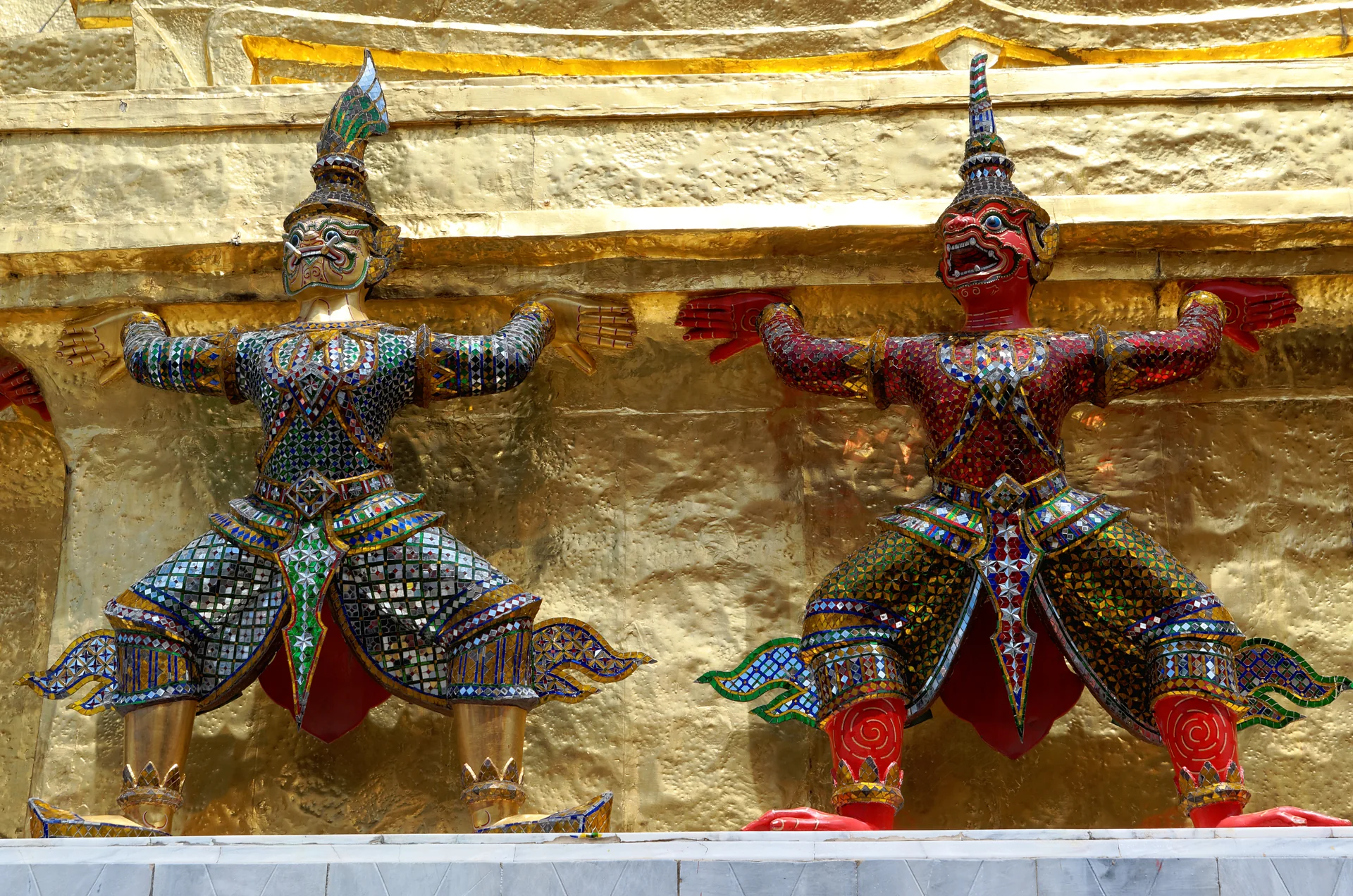 Duas figuras coloridas do Ramakien sustentam uma estrutura dourada no templo Wat Phra Kaew, em Bangkok.