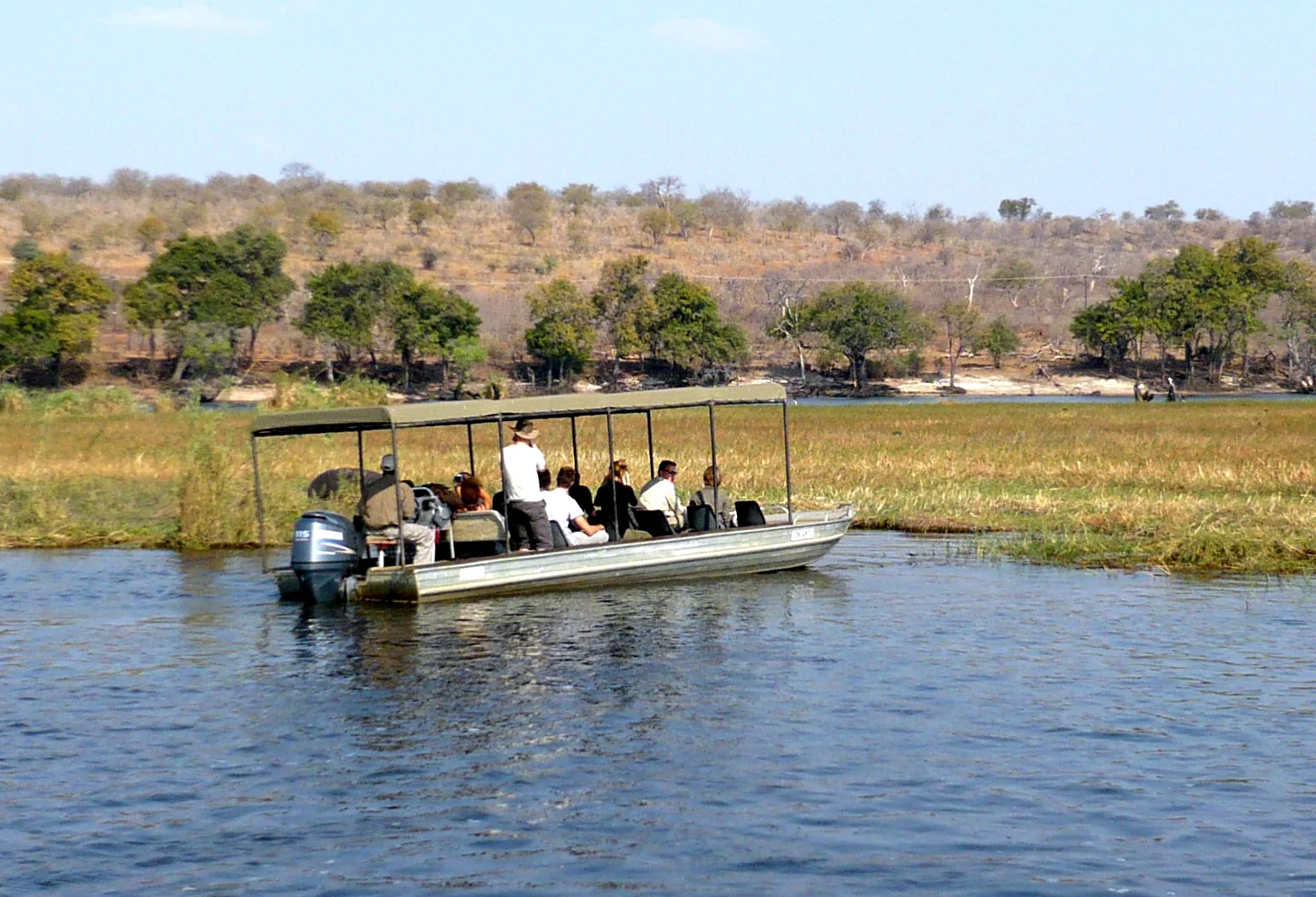 Barco de observação turística navega no rio Chobe diante de vegetação ribeirinha