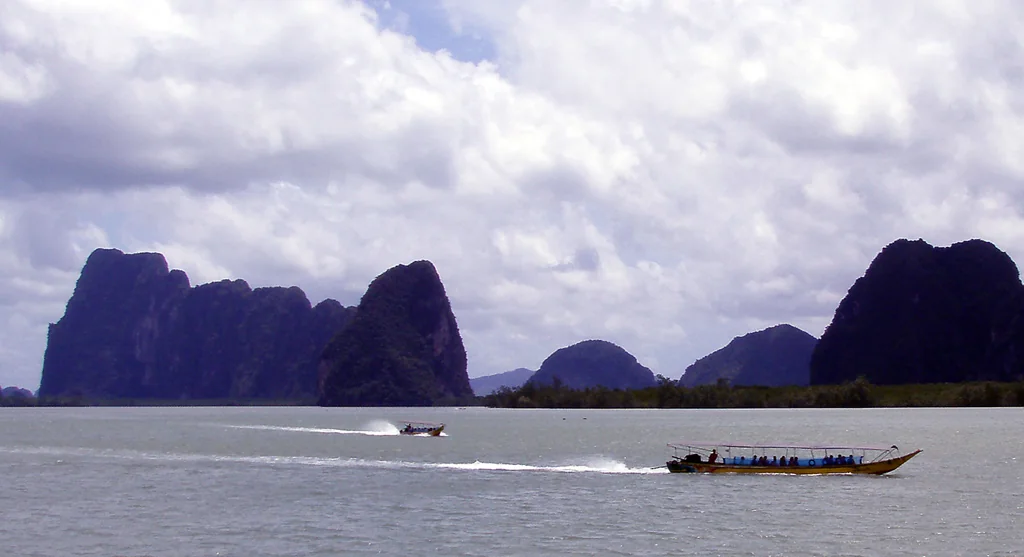 Barcos long-tail navegando entre ilhas rochosas da baía de Phang Nga.