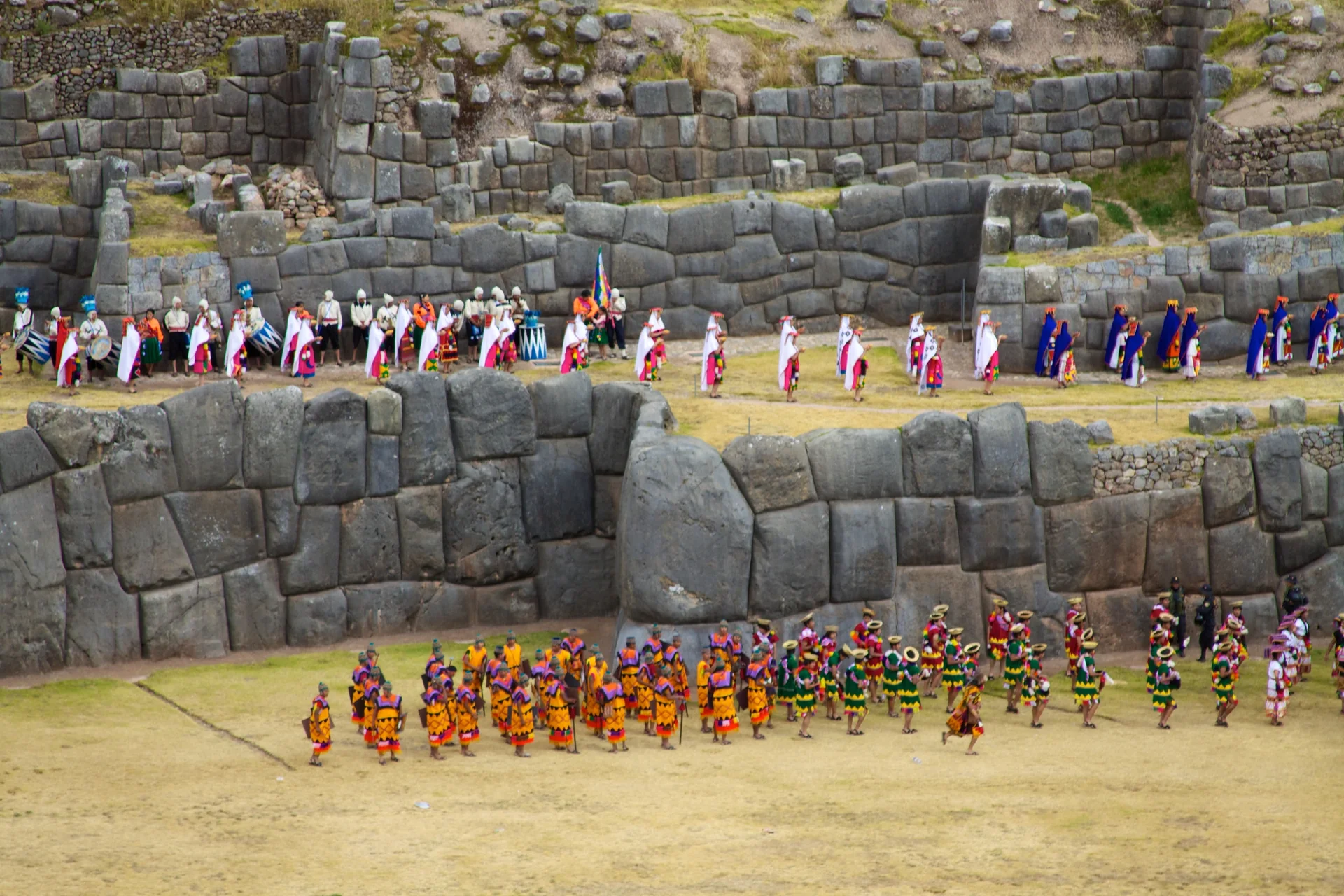 Participantes do Inti Raymi diante de paredes de pedra em Saqsaywaman, Cusco.
