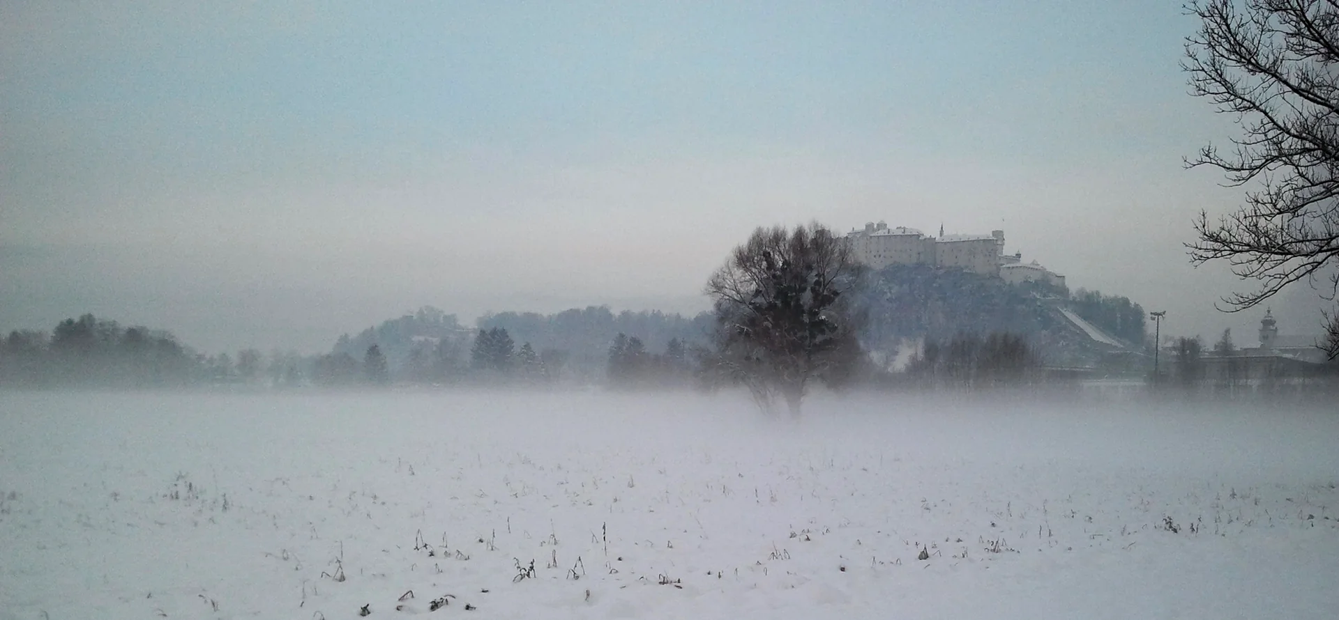 Fortaleza Hohensalzburg vista além de um campo coberto de neve em um dia de inverno.