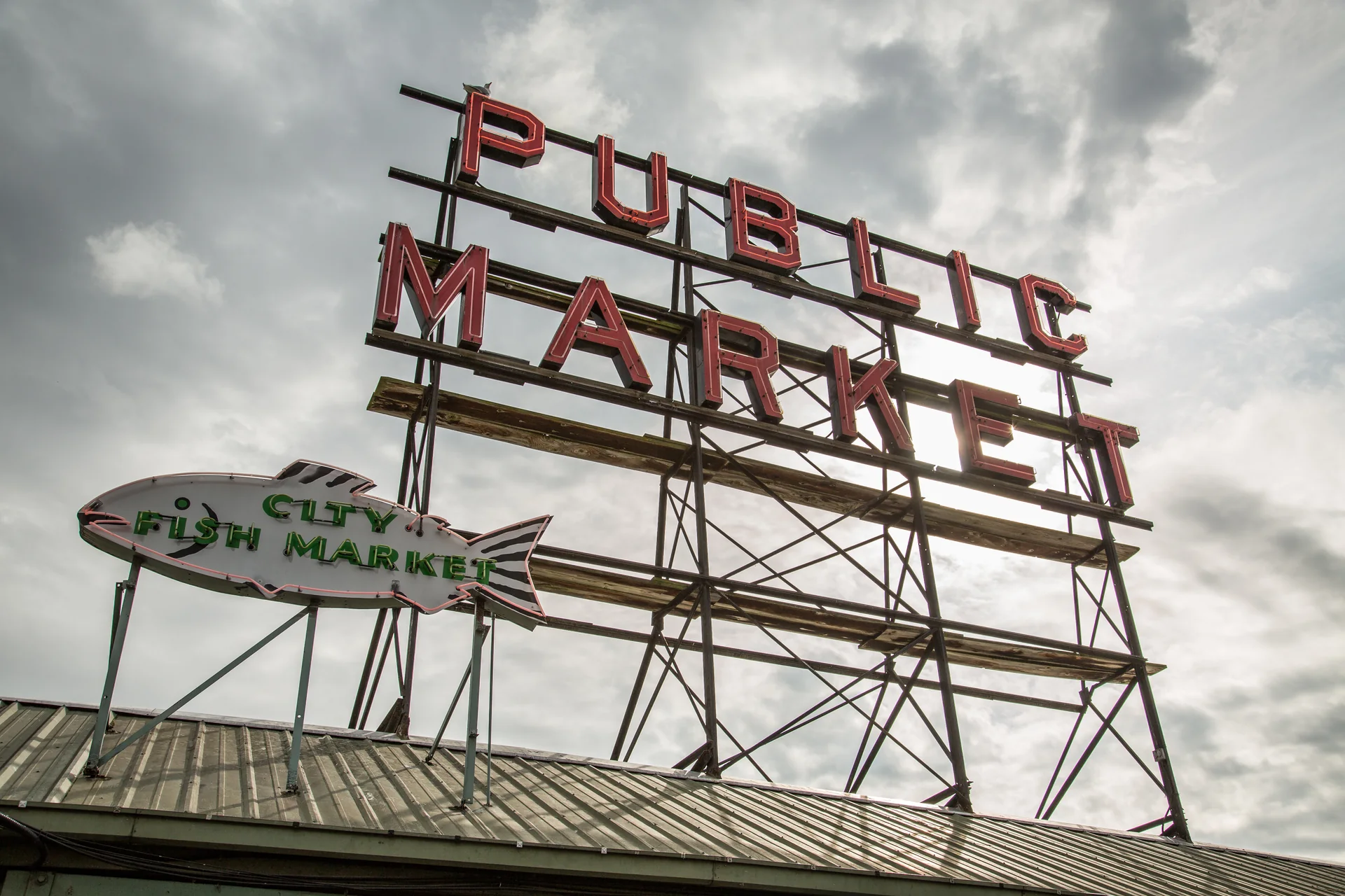 Letreiro Public Market e placa em forma de peixe do Pike Place Market sob céu nublado.