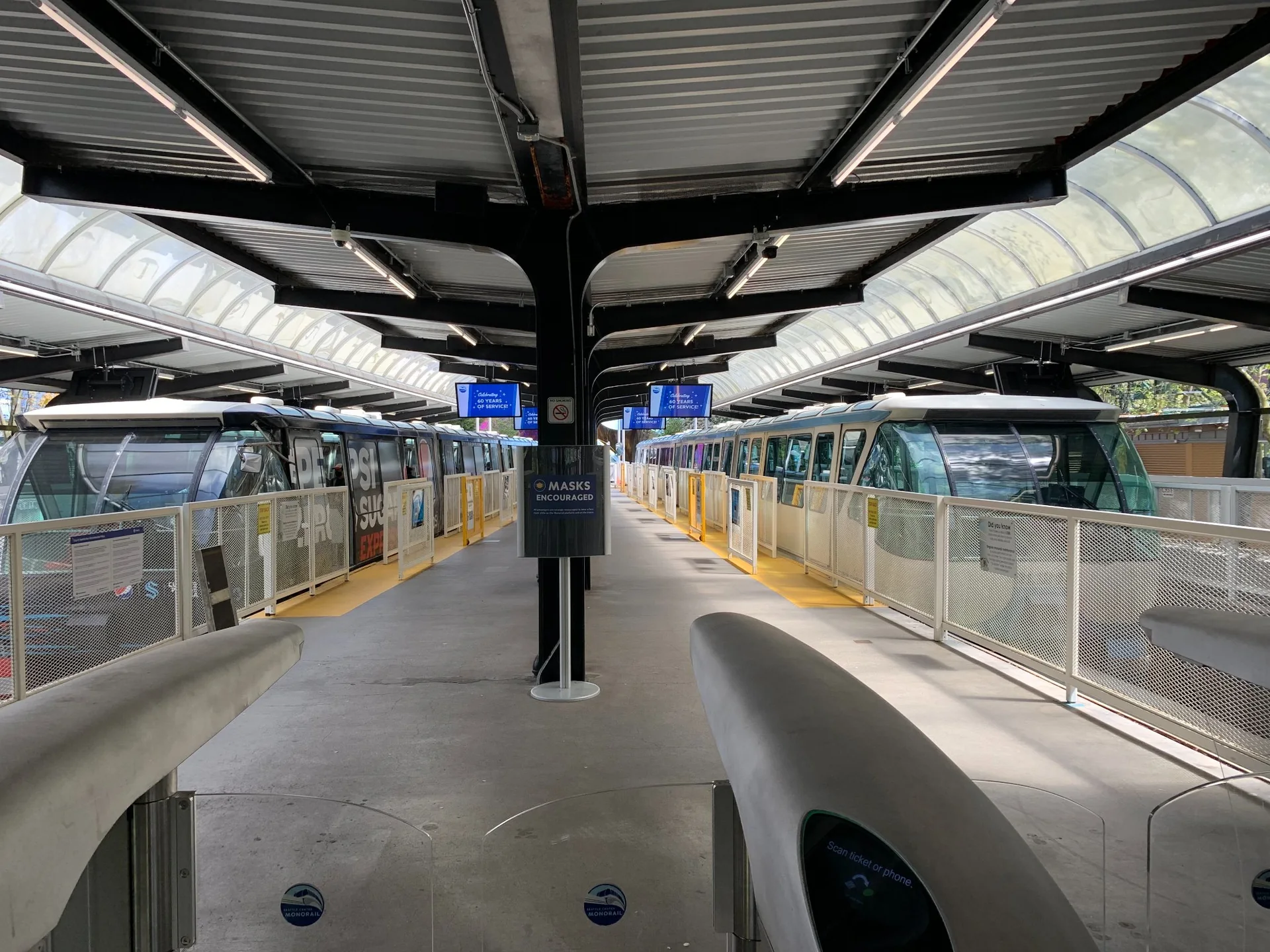 Plataforma da estação do Seattle Center Monorail com dois trens prateados e estruturas metálicas.