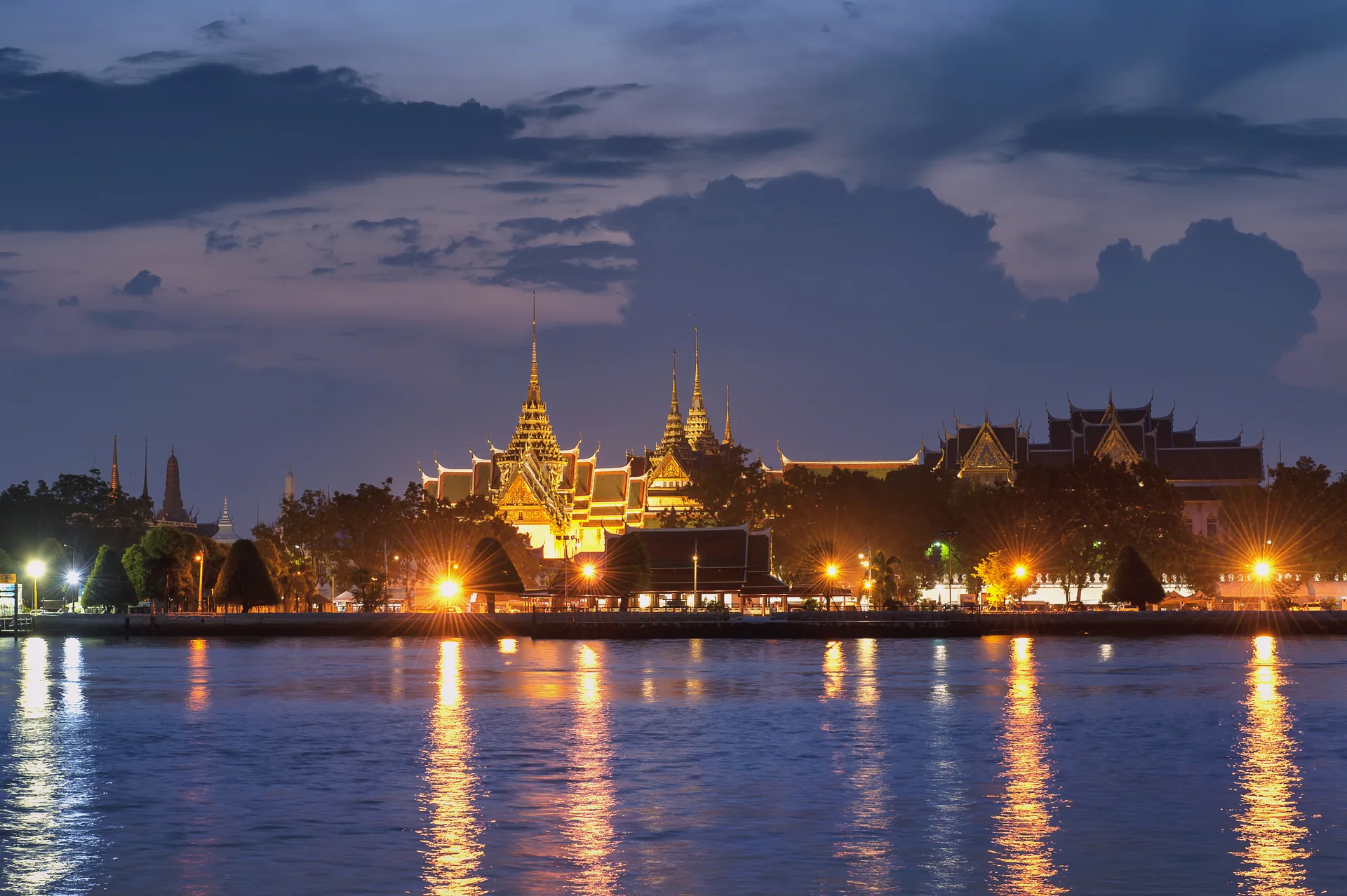 Complexo iluminado de Wat Phra Kaew, em Bangkok, refletido nas águas do rio ao entardecer.