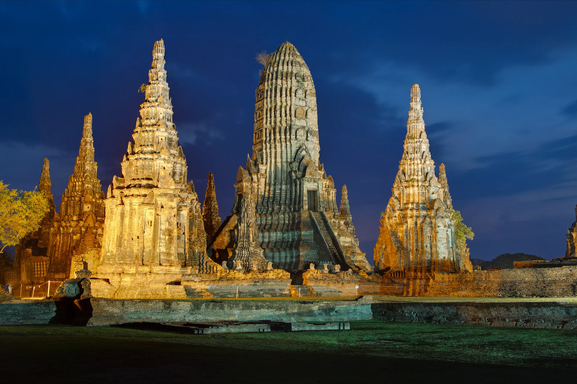 Torres e estruturas históricas iluminadas de Wat Chai Watthanaram, em Ayutthaya, sob céu azul escuro.