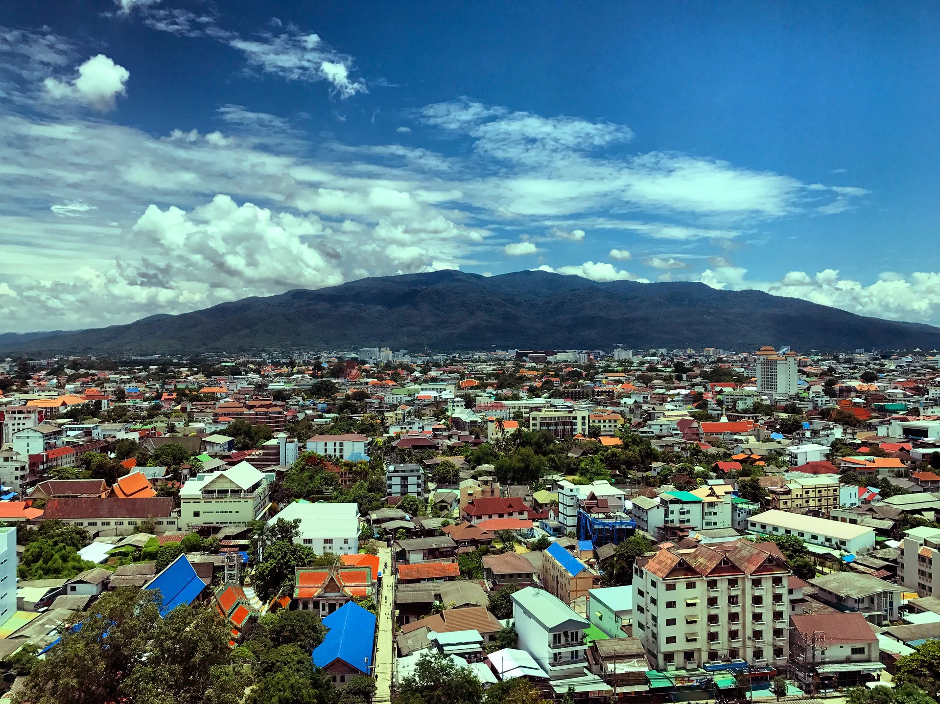 Vista urbana de Chiang Mai com a montanha Doi Suthep ao fundo, sob nuvens.
