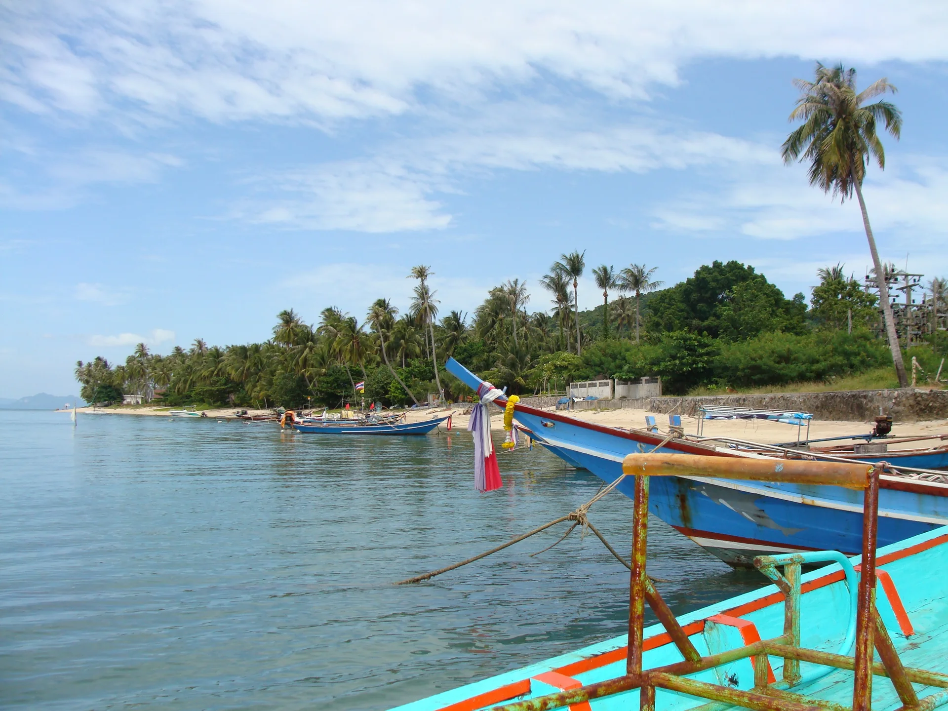 Barcos de madeira ancorados junto a uma praia com coqueiros em Koh Samui.