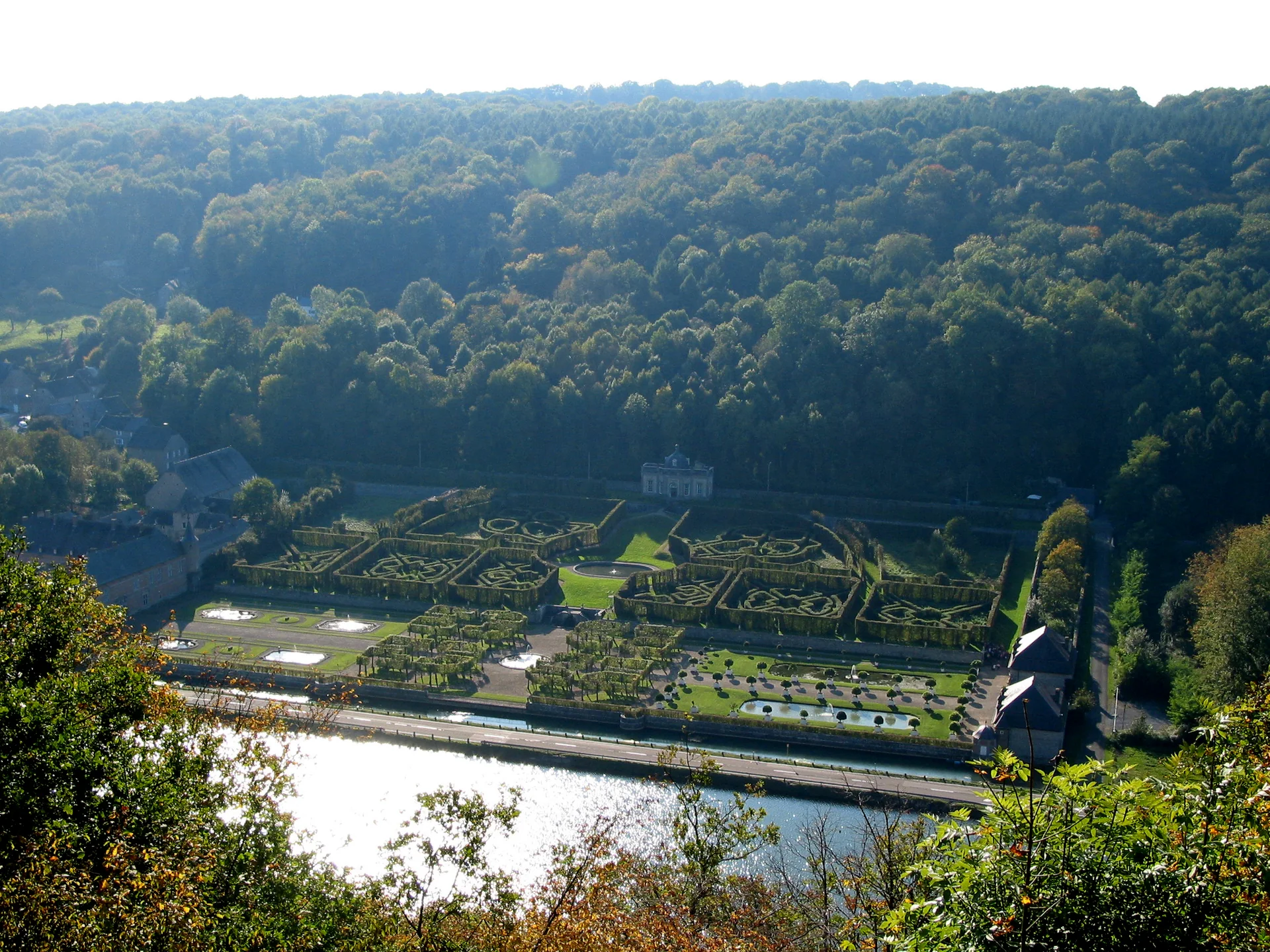 Vista elevada do Castelo de Freÿr, de seus jardins geométricos e do rio Mosa, cercados por mata.