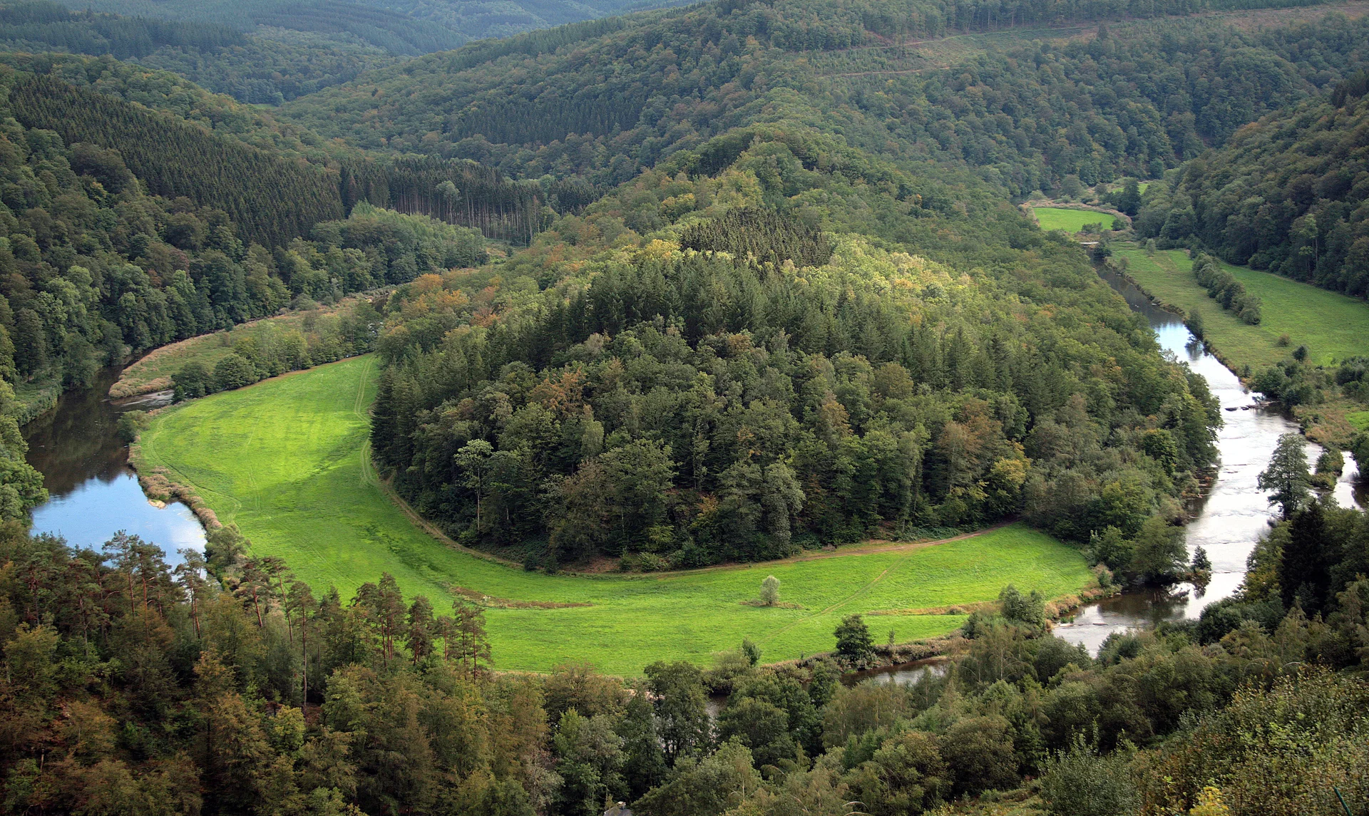 Vista panorâmica do meandro do rio Semois em torno do Tombeau du Géant, entre encostas cobertas de floresta e prados.