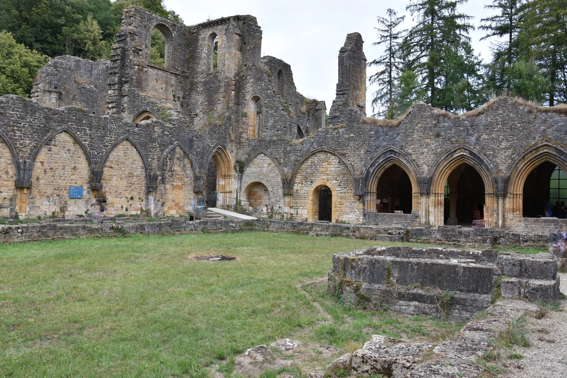 Arcadas de pedra e ruínas da antiga Abadia de Orval, com gramado no pátio.