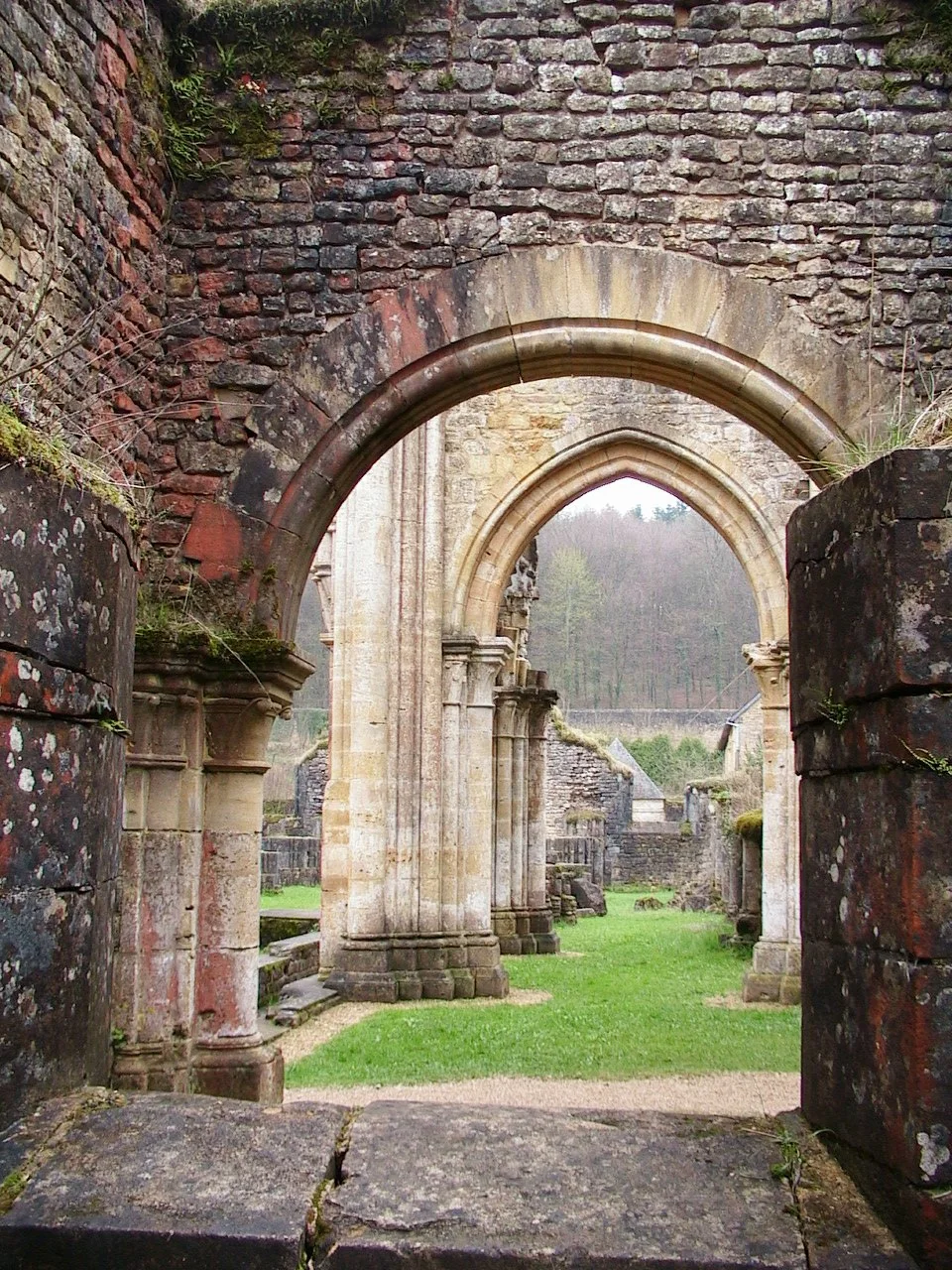 Nave arruinada da antiga igreja abacial de Orval, com arcadas de pedra e vegetação ao fundo.