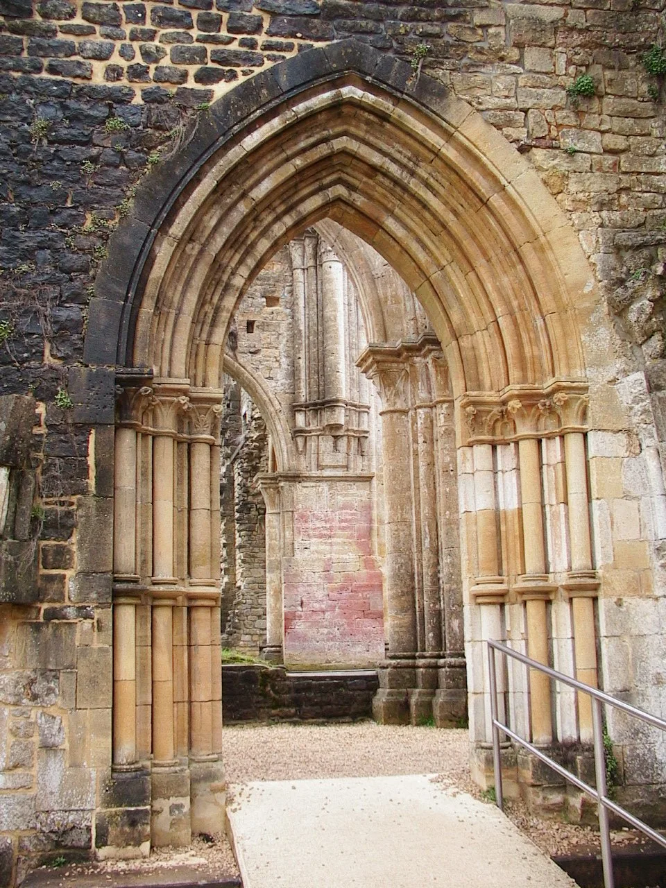 Detalhe do claustro em ruínas da Abadia de Orval, com arcos de pedra e caminho interno.