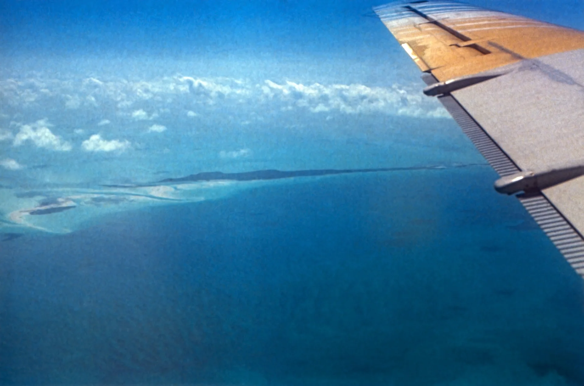 Ilhas e bancos de areia das Exumas vistos de um avião, com asa ao lado e o mar em tons de azul.