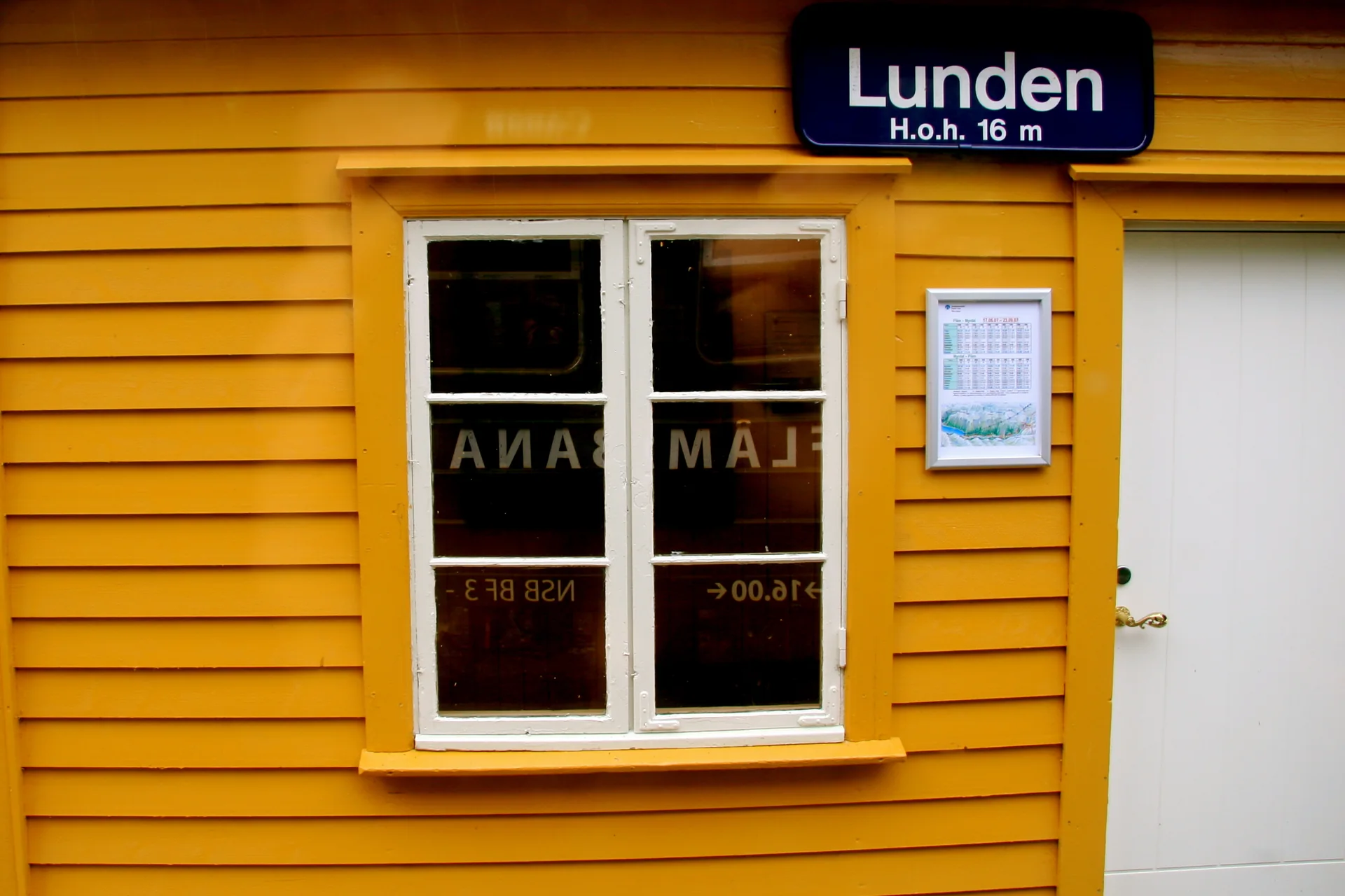 Pequena estação amarela de Lunden junto aos trilhos da Flåmsbana, com encosta verde ao fundo.