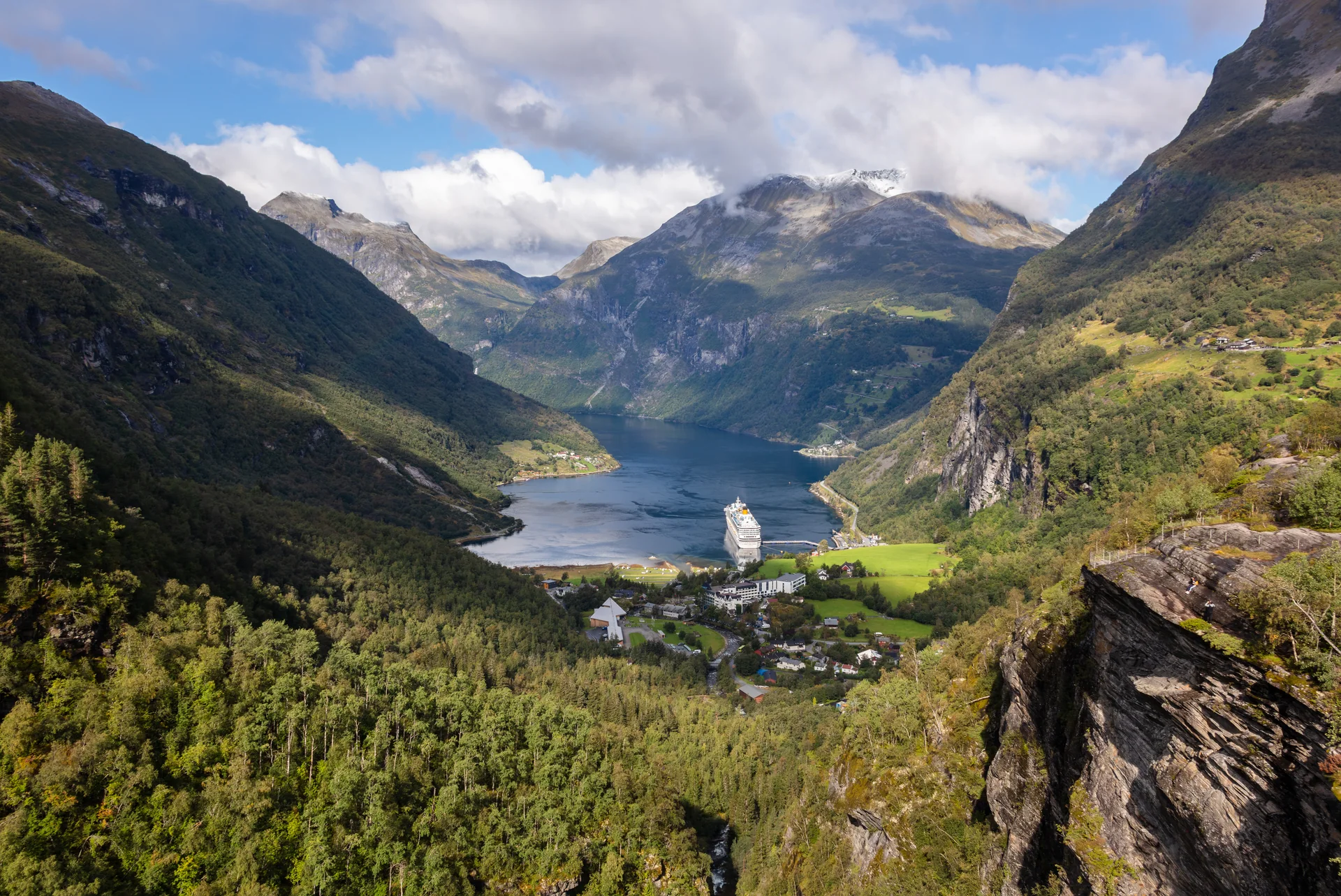 Geirangerfjord e a vila de Geiranger vistos do mirante Flydalsjuvet sob céu claro e luz natural.
