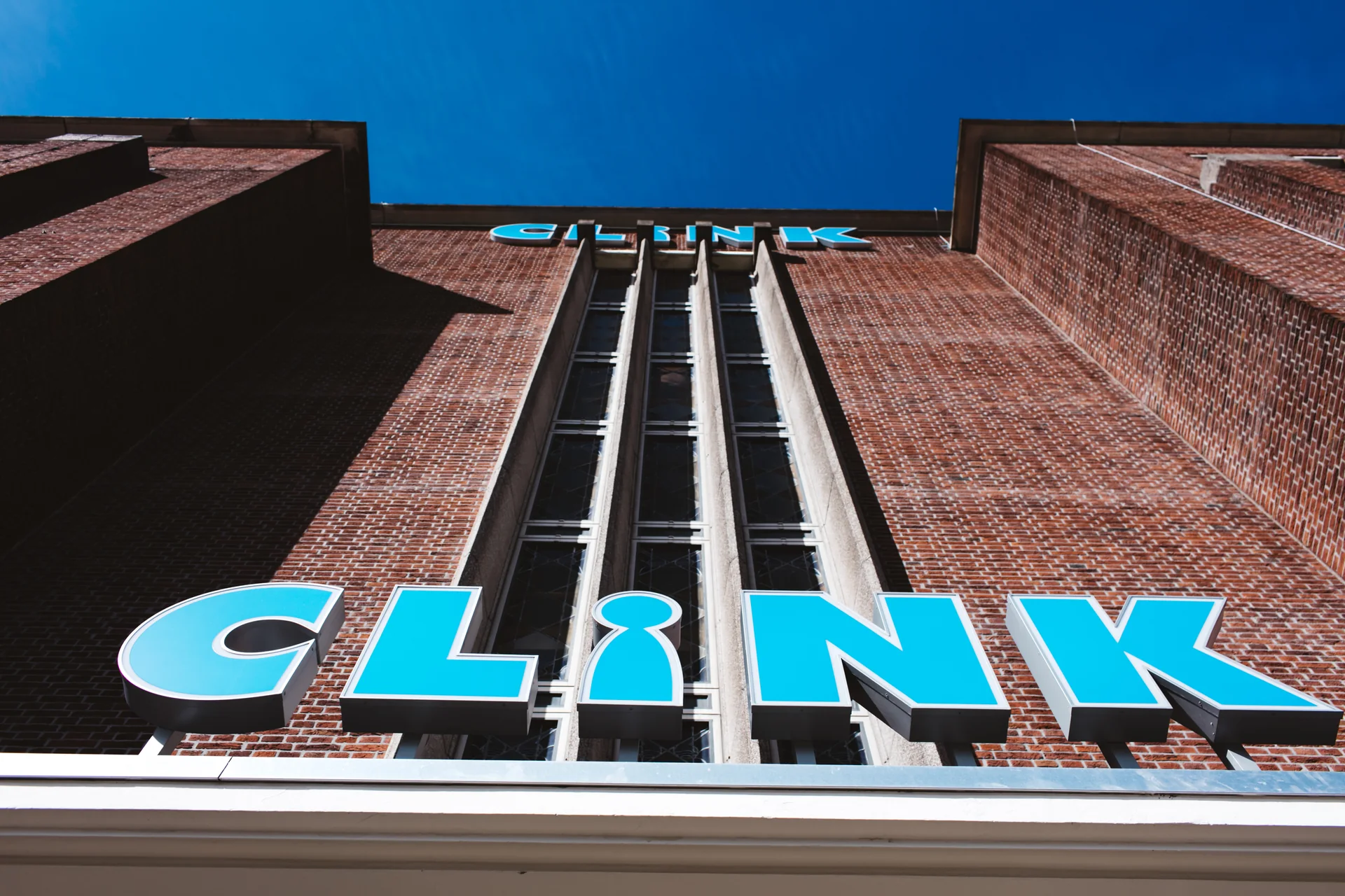 Fachada de tijolos do ClinkNOORD em Amsterdam, vista de baixo contra um céu azul intenso.