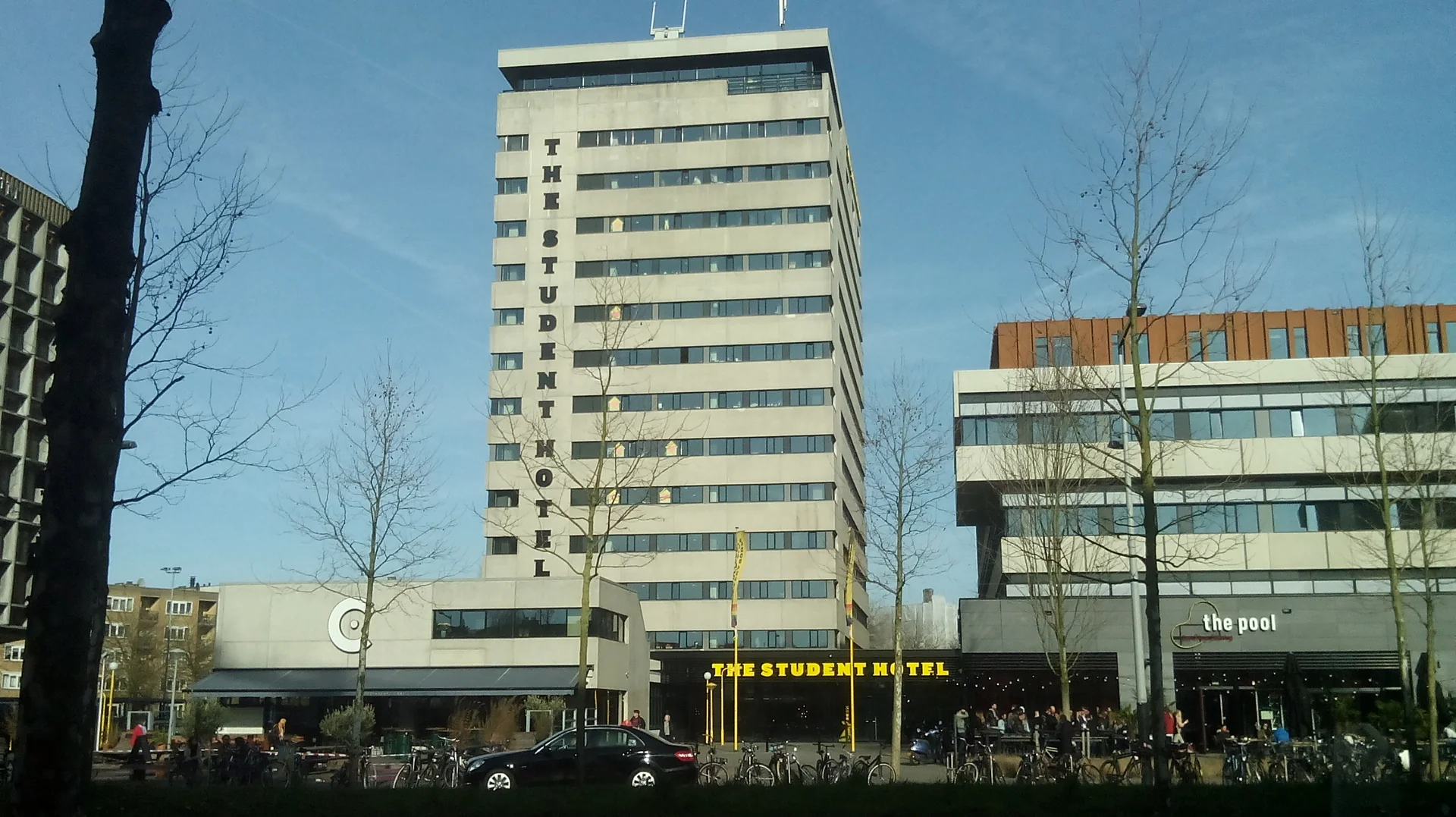 Edifício alto com a antiga placa The Student Hotel na Wibautstraat, sob céu azul em Amsterdam.