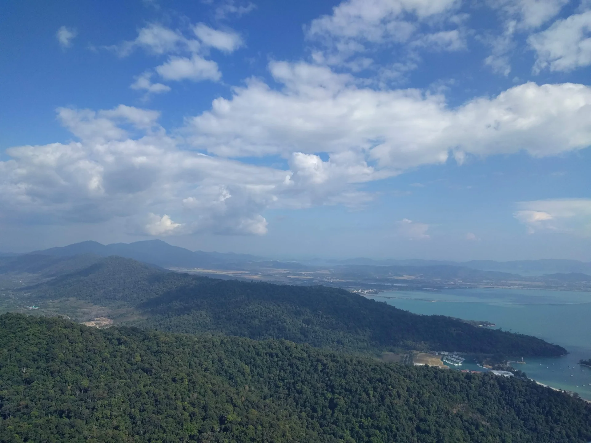 Panorama ensolarado de Langkawi visto da serra de Machinchang, com floresta, ilhas e mar ao fundo.
