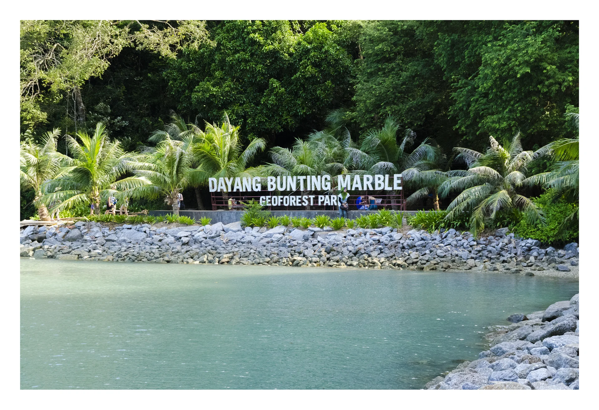 Margem do Dayang Bunting Marble Geoforest Park, com vegetação tropical e água turquesa.