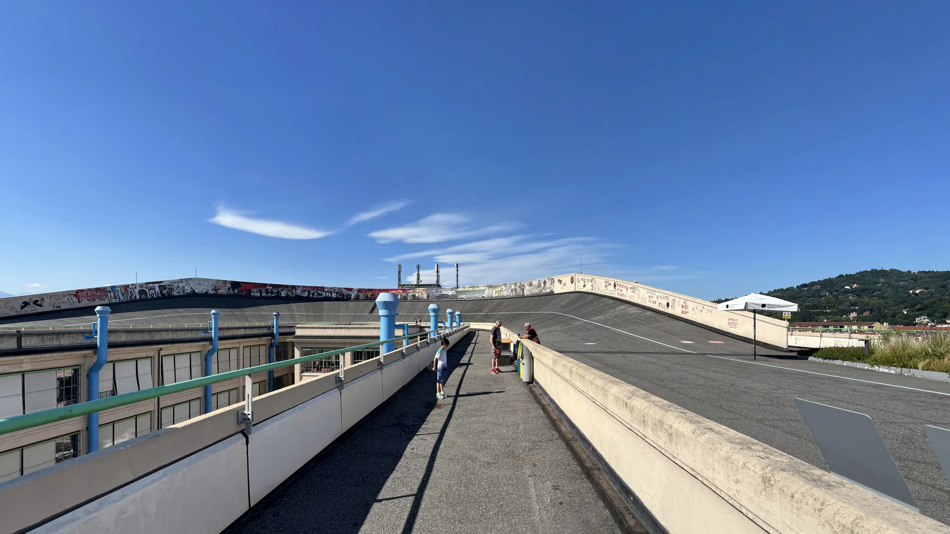 Curva inclinada da antiga pista de testes da FIAT no telhado do Lingotto, com visitantes e colinas de Turim ao fundo