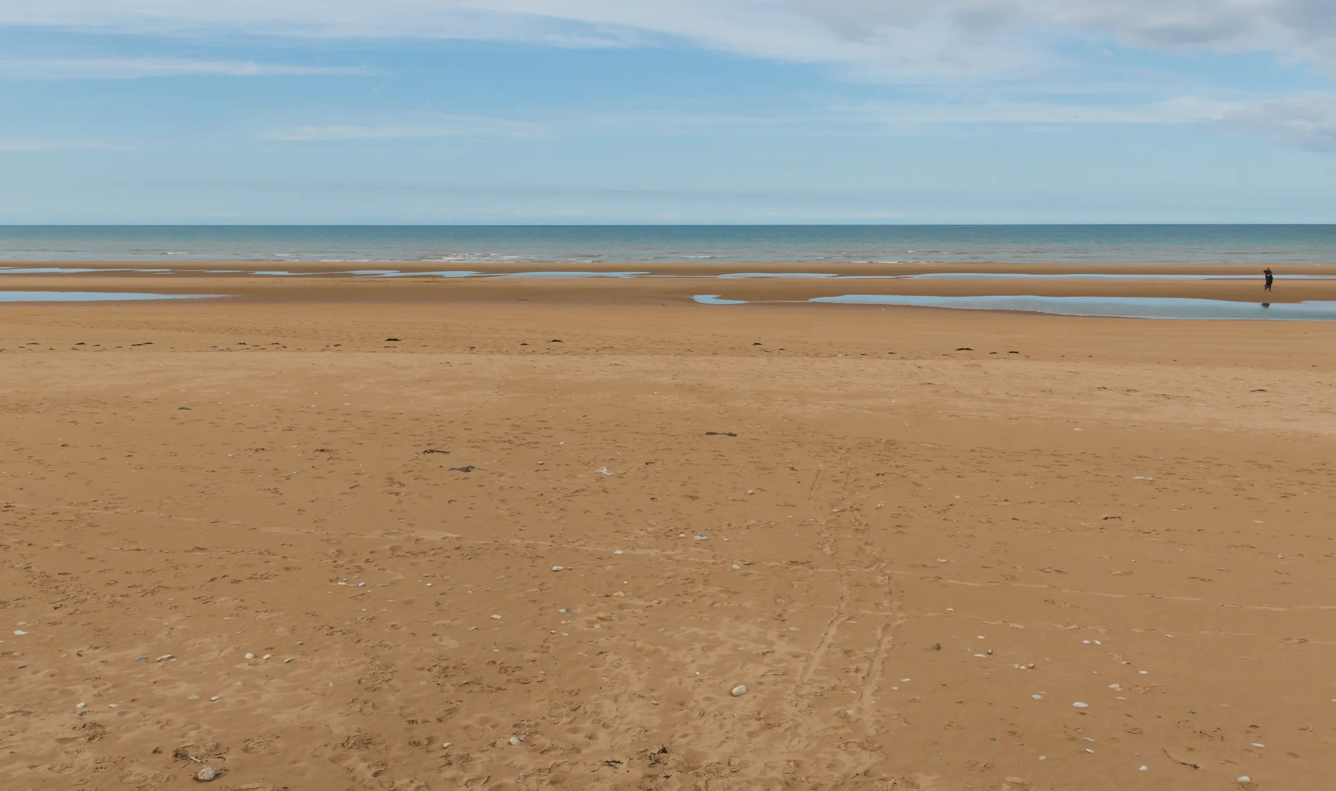 Faixa de areia e mar de Omaha Beach sob céu aberto, na costa da Normandia