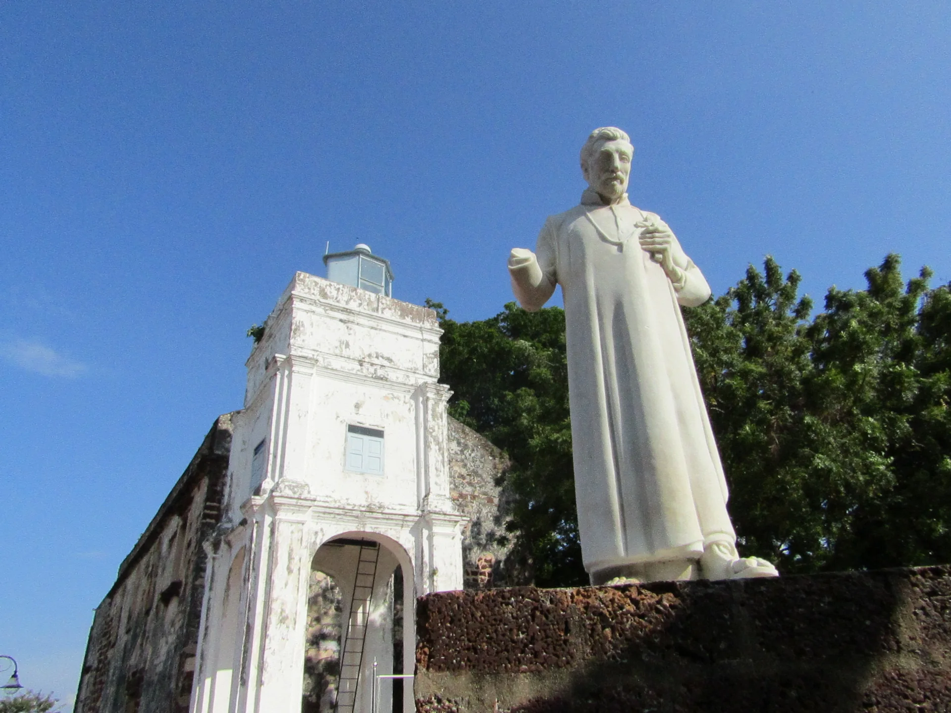 Estátua de Francisco Xavier junto às ruínas da Igreja de São Paulo em Melaka sob céu azul.