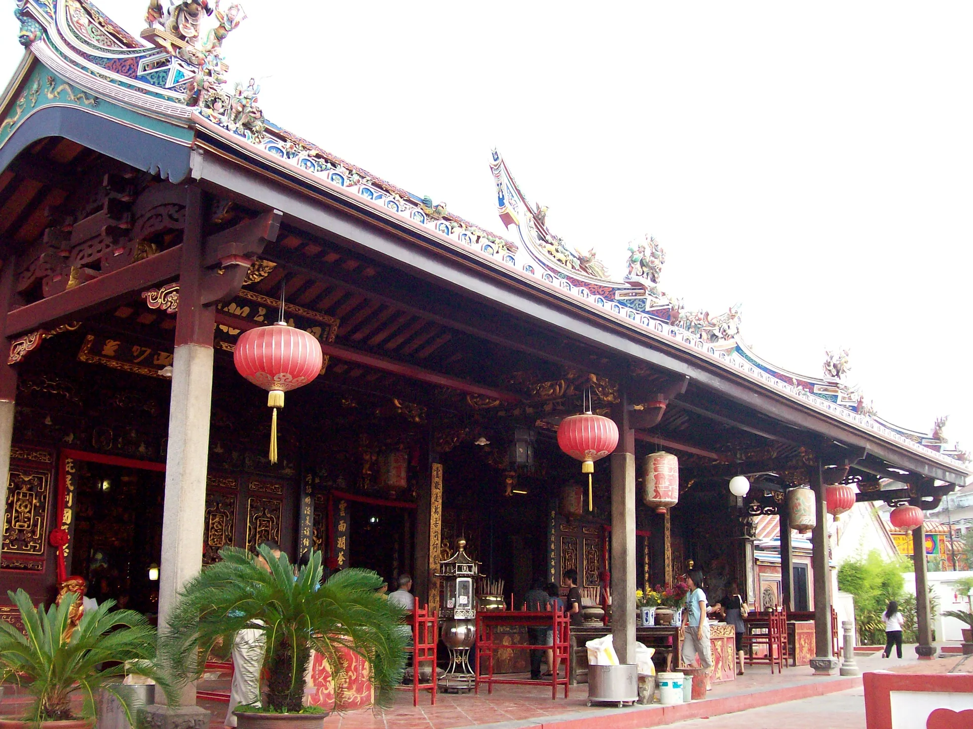 Fachada ornamentada do Templo Cheng Hoon Teng em Melaka, com lanternas vermelhas à luz do dia.