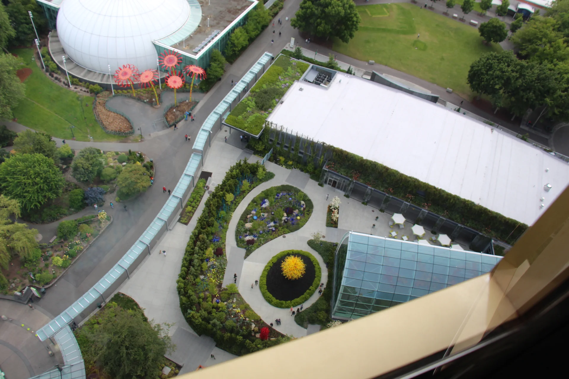 Vista elevada do Chihuly Garden and Glass, com jardim, esculturas coloridas e caminhos ao lado da Space Needle.