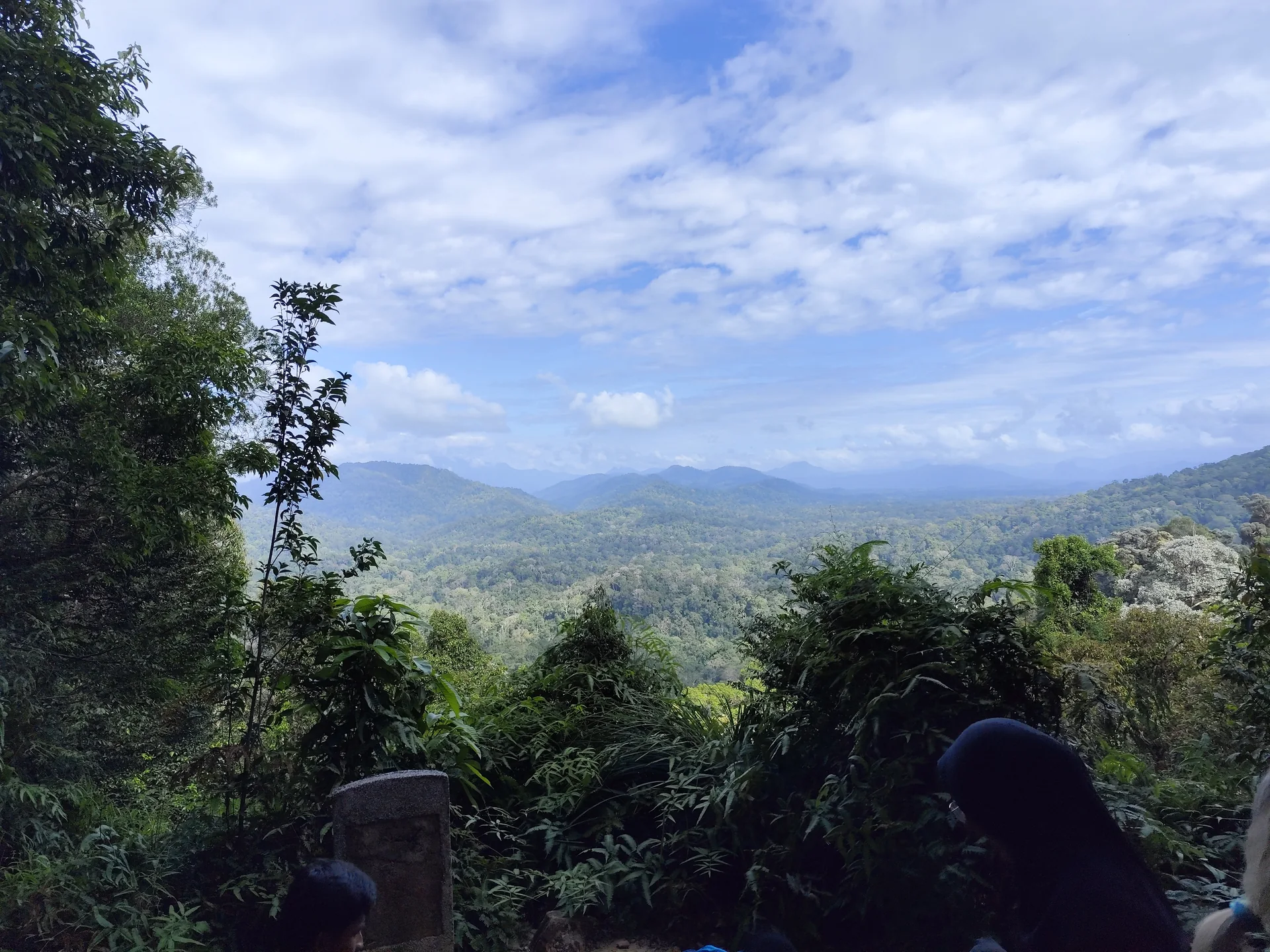 Vista ampla de colinas cobertas por floresta em Taman Negara sob céu parcialmente nublado.