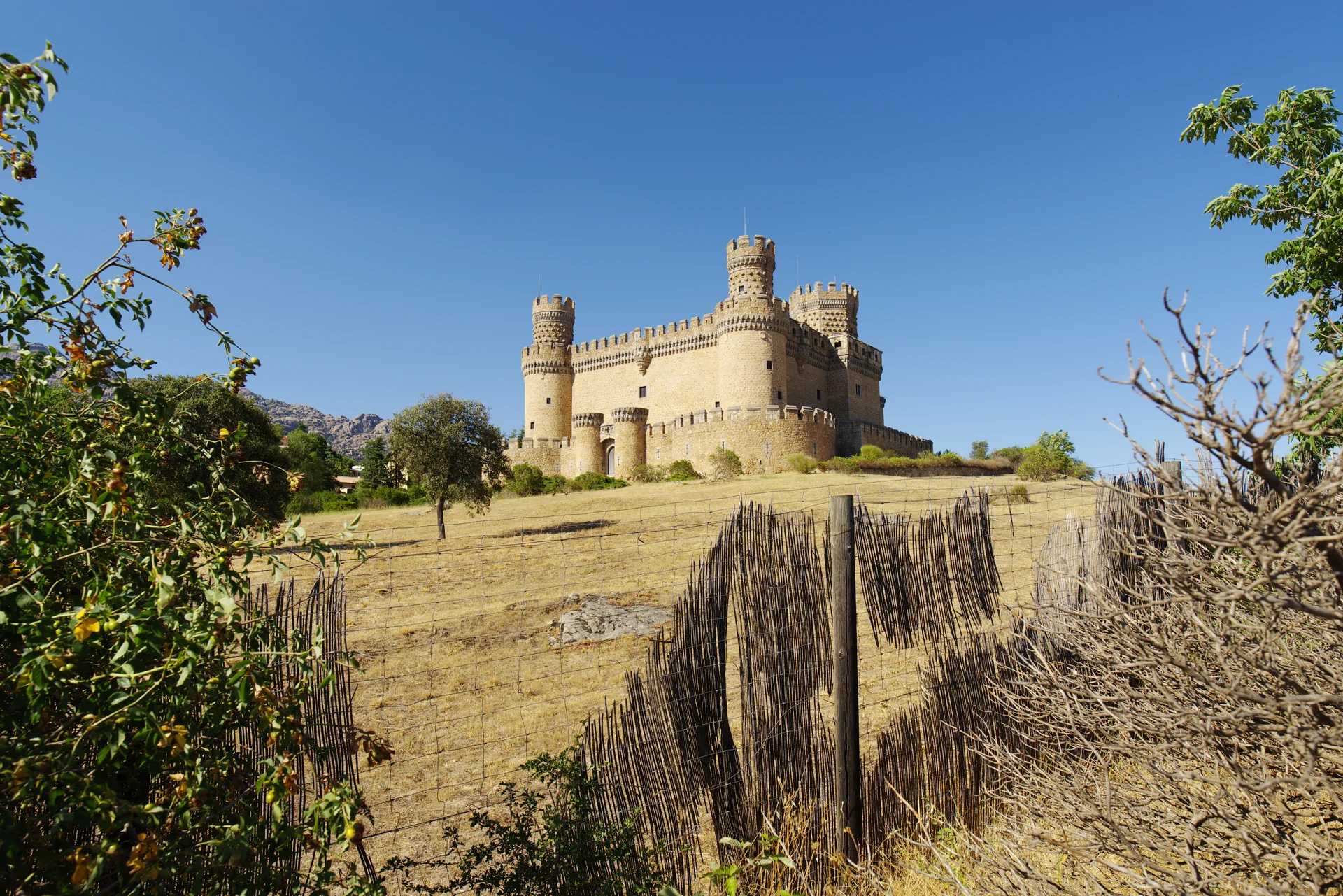 Castelo de Manzanares el Real com torres ameadas, visto de um caminho gramado.