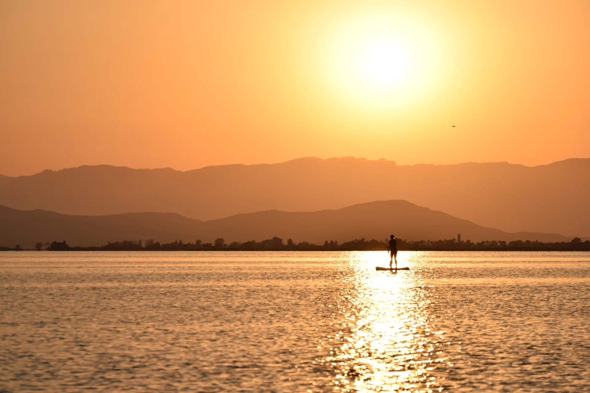 Pessoa em pé sobre prancha ao entardecer nas águas do Parque Natural do Delta do Ebro, perto de La Ràpita.