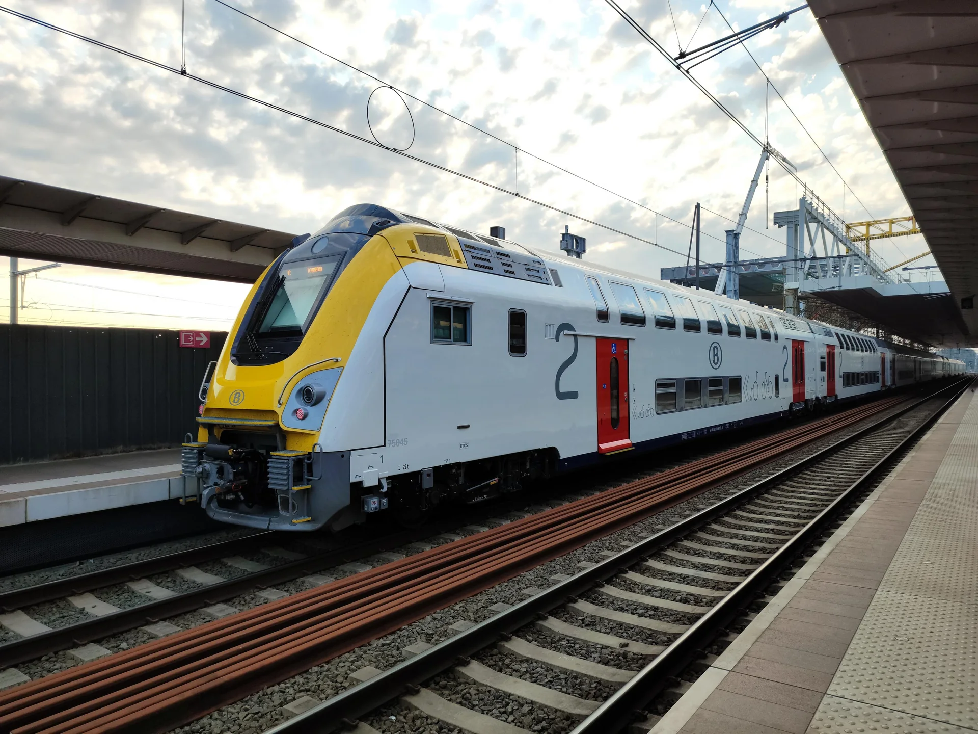 Trem intermunicipal de dois andares da NMBS/SNCB parado em plataforma de Gante sob luz natural.