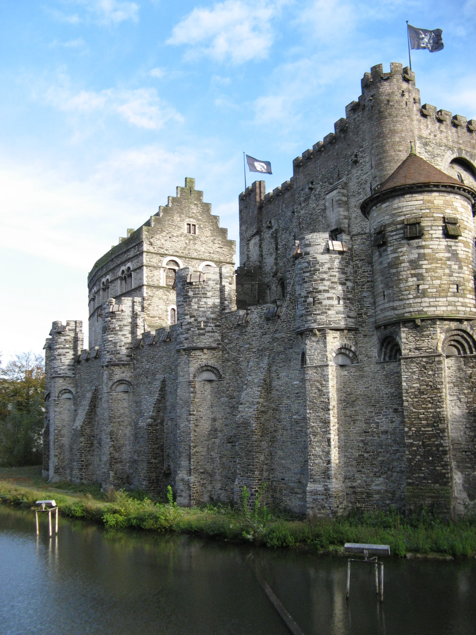 Fachada de pedra, torres e fosso do Castelo dos Condes, Gravensteen, em Gante sob luz natural.