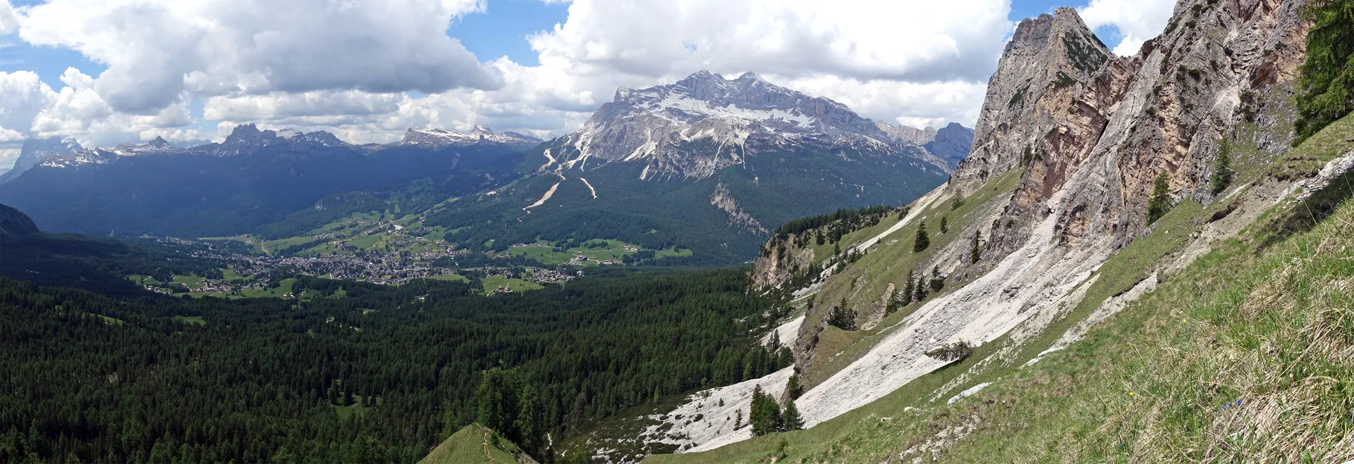 Vista panorâmica de Cortina d’Ampezzo entre vale arborizado e montanhas das Dolomitas em dia claro.