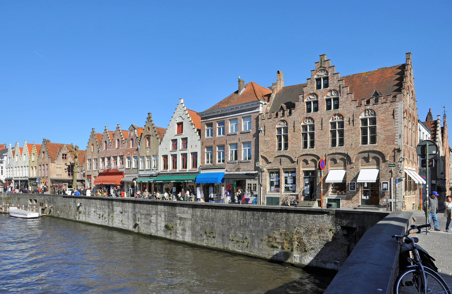 Casario histórico junto ao canal da Rozenhoedkaai, em Bruges, sob céu azul e luz diurna.