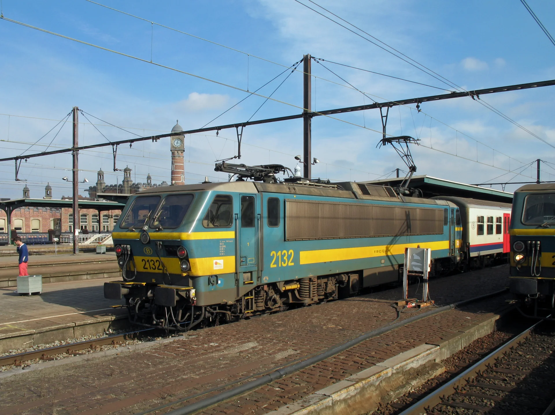 Locomotiva SNCB/NMBS na estação Gent-Sint-Pieters, com a torre do relógio ao fundo sob céu azul.
