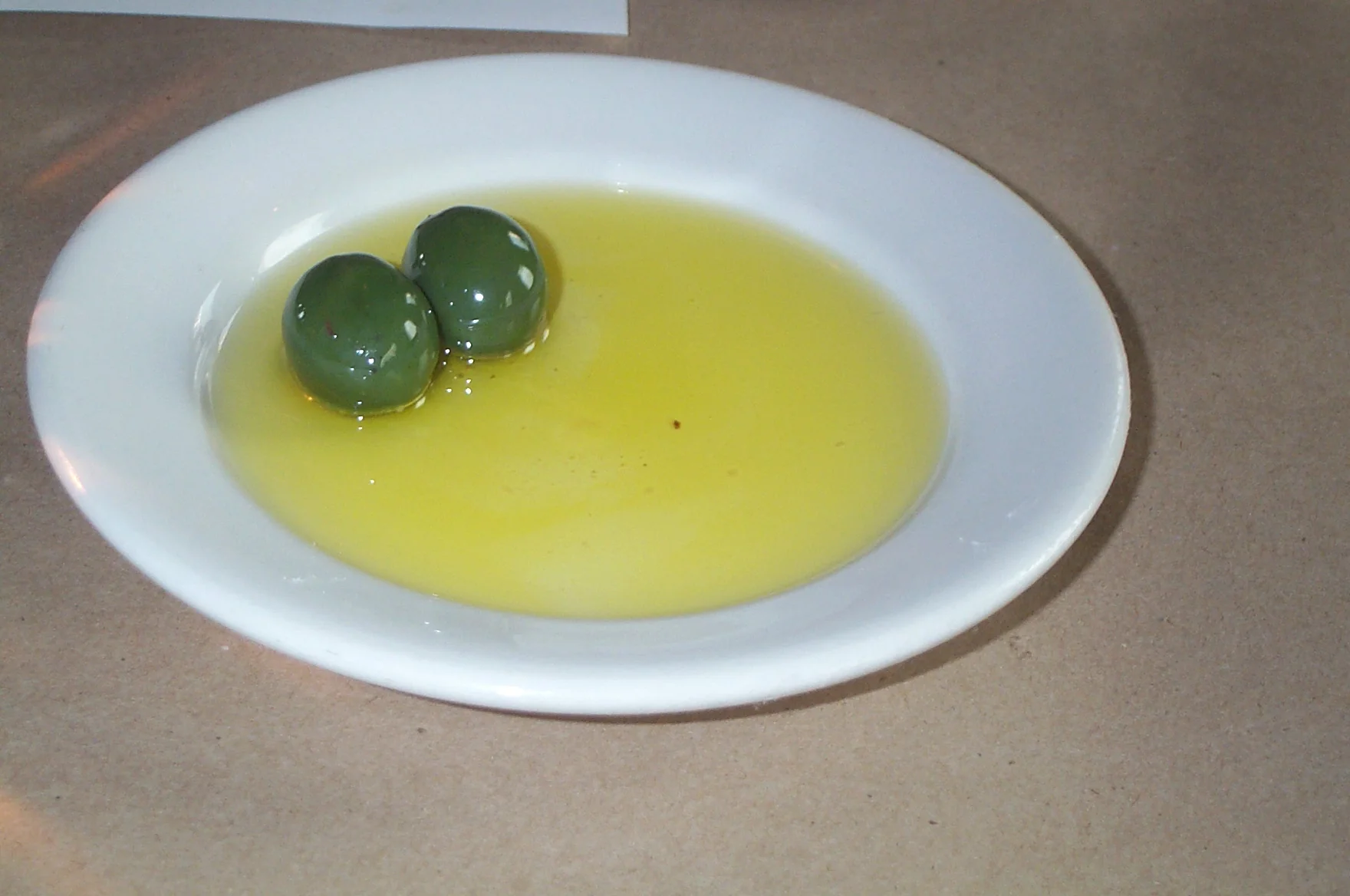 Azeitonas verdes em azeite numa pequena tigela branca, sem rótulo de marca.