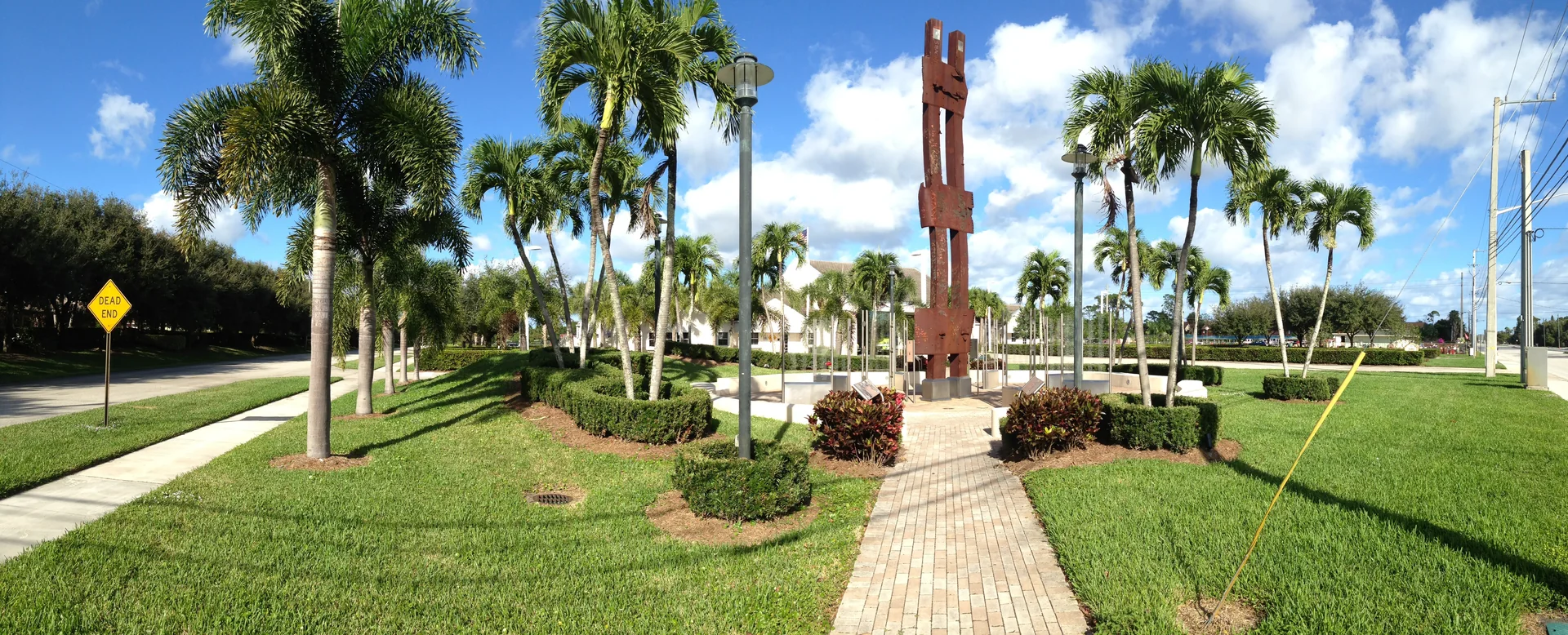 Calçadão arborizado de Palm Beach Gardens com palmeiras e céu azul.