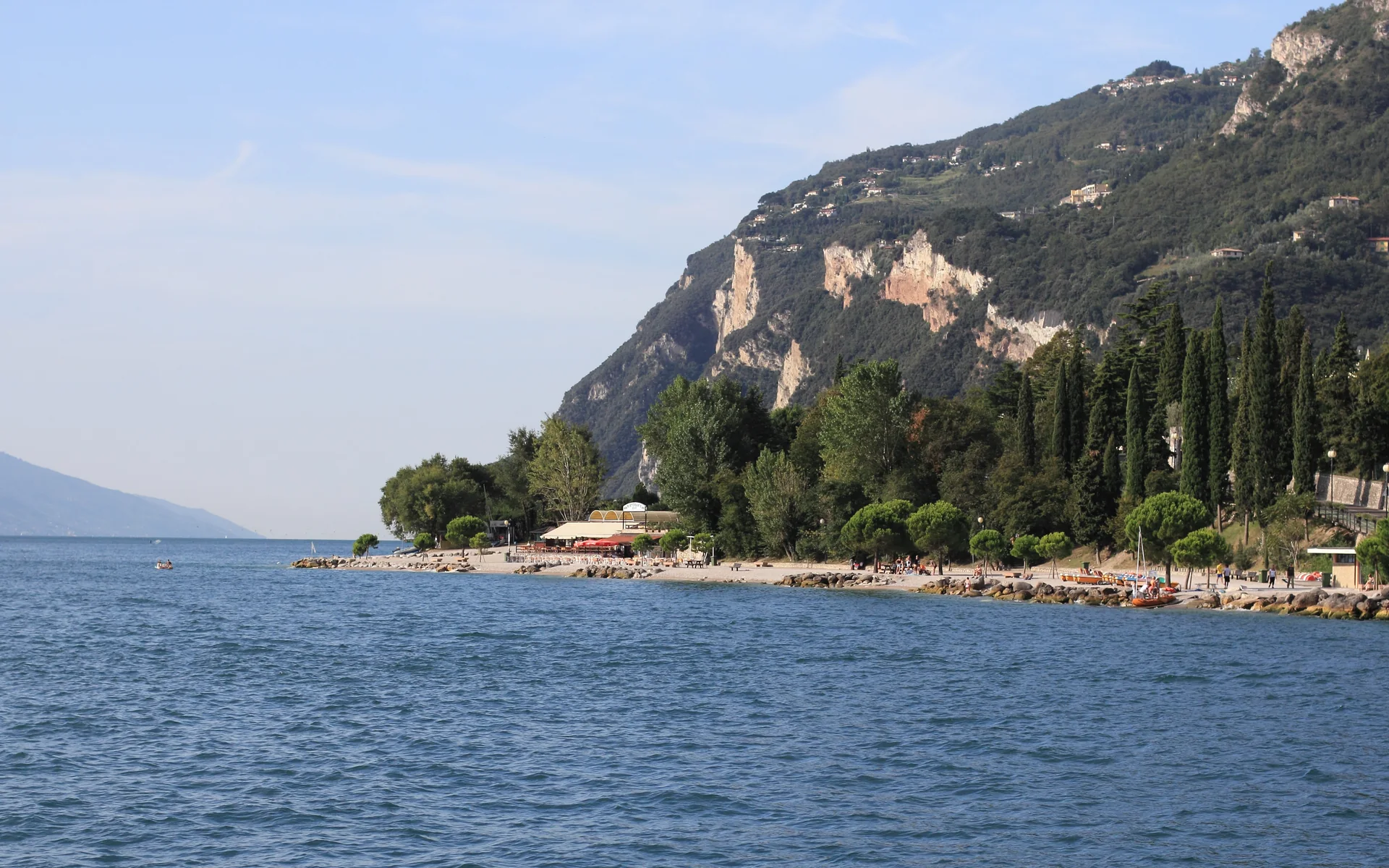 Praia de Limone sul Garda com faixa de seixos, água do lago e encosta montanhosa ao fundo.