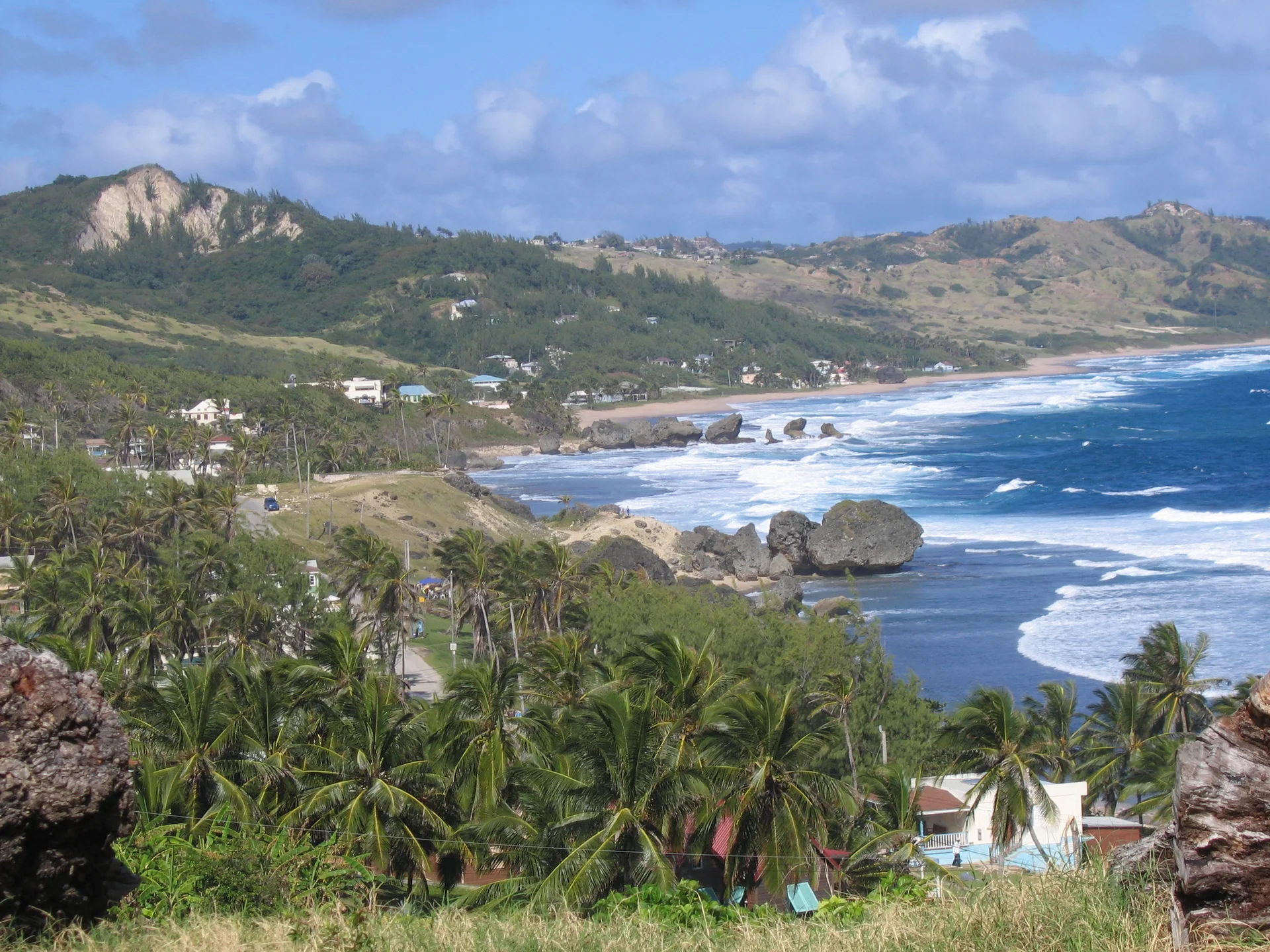 Vista ampla e elevada de Bathsheba, em Barbados, com ondas do Atlântico, rochas escuras e palmeiras.