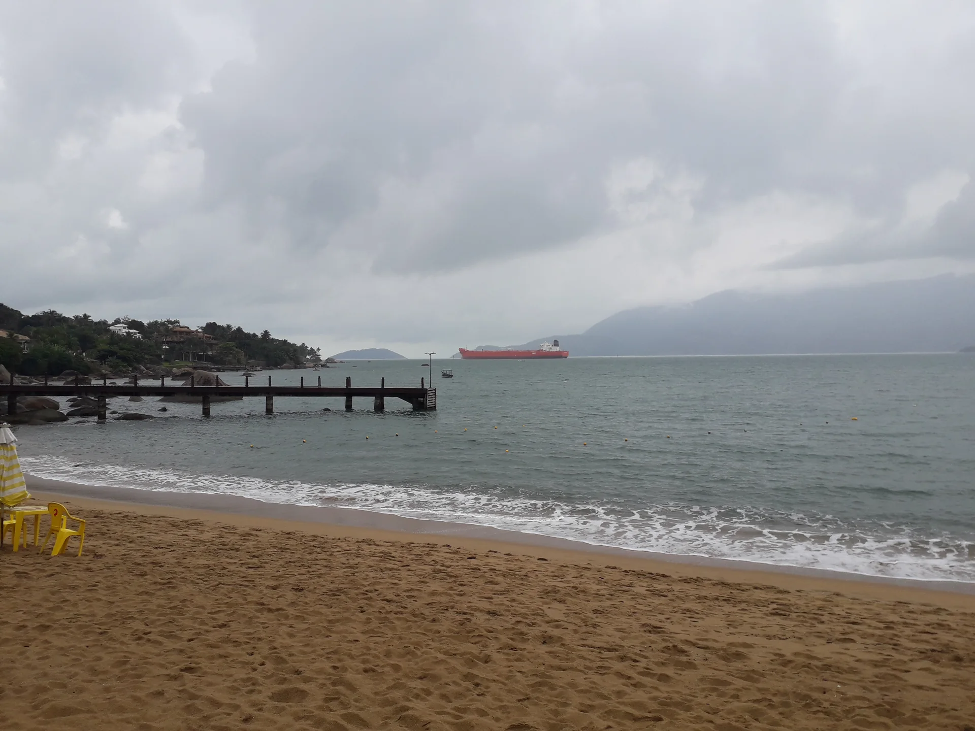 Vista diurna da Praia Grande em Ilhabela, com faixa de areia, mar e montanhas cobertas por vegetação.