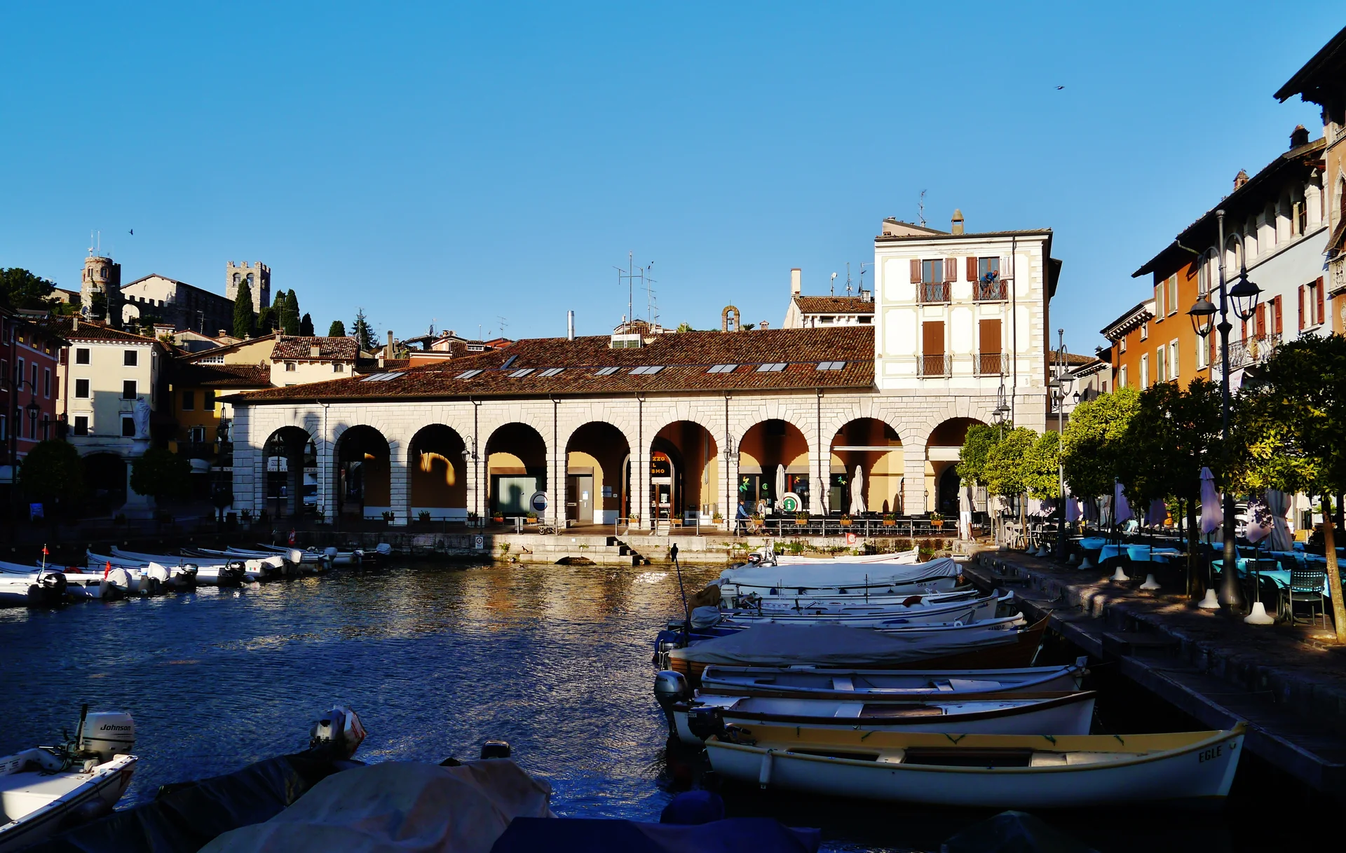 Porto Vecchio de Desenzano del Garda em luz diurna, com pequenas embarcações, fachadas históricas e água do lago.