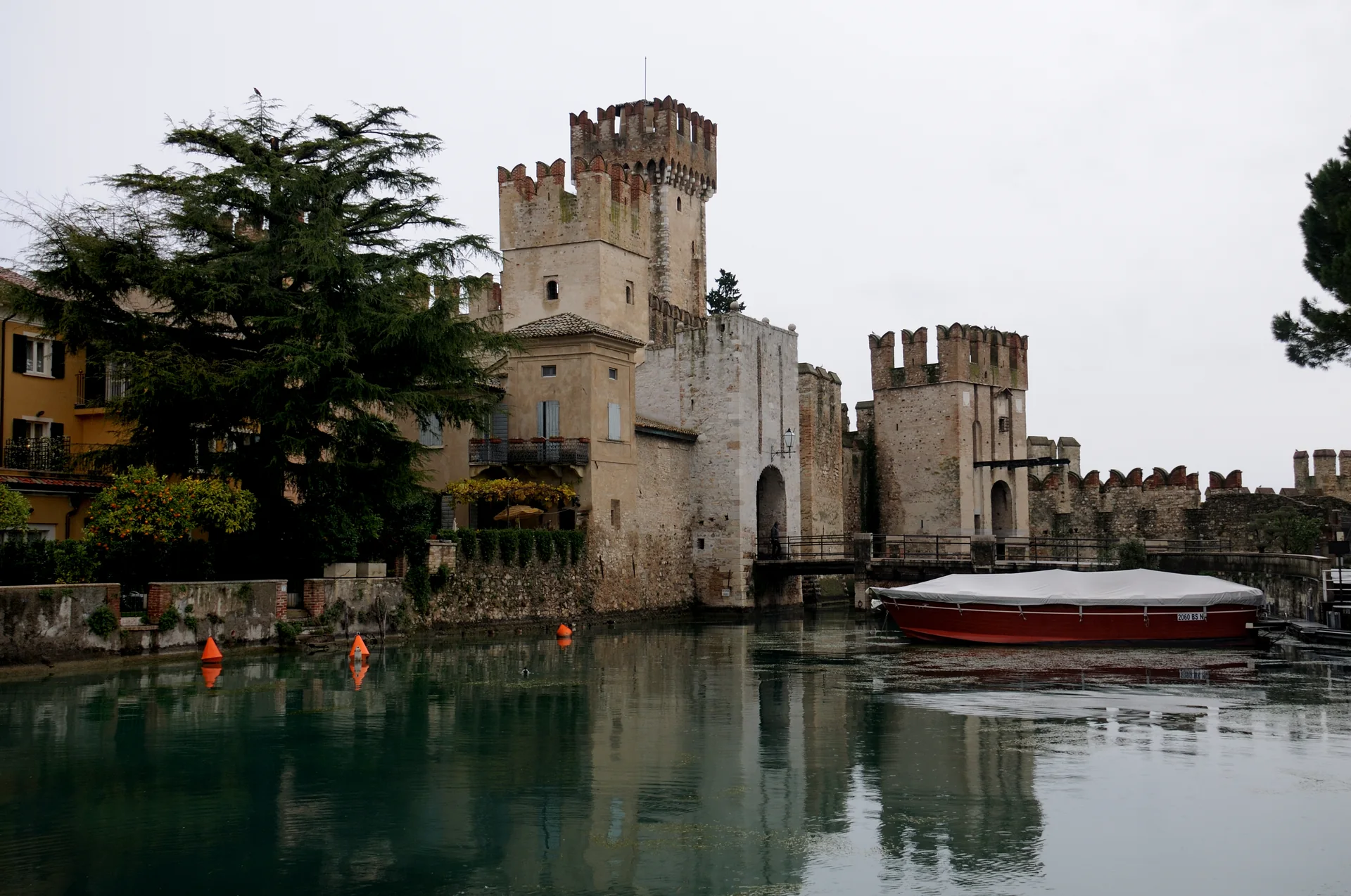 Castello Scaligero e porto fortificado de Sirmione em luz natural, vistos do canal com água e embarcação ao primeiro plano.