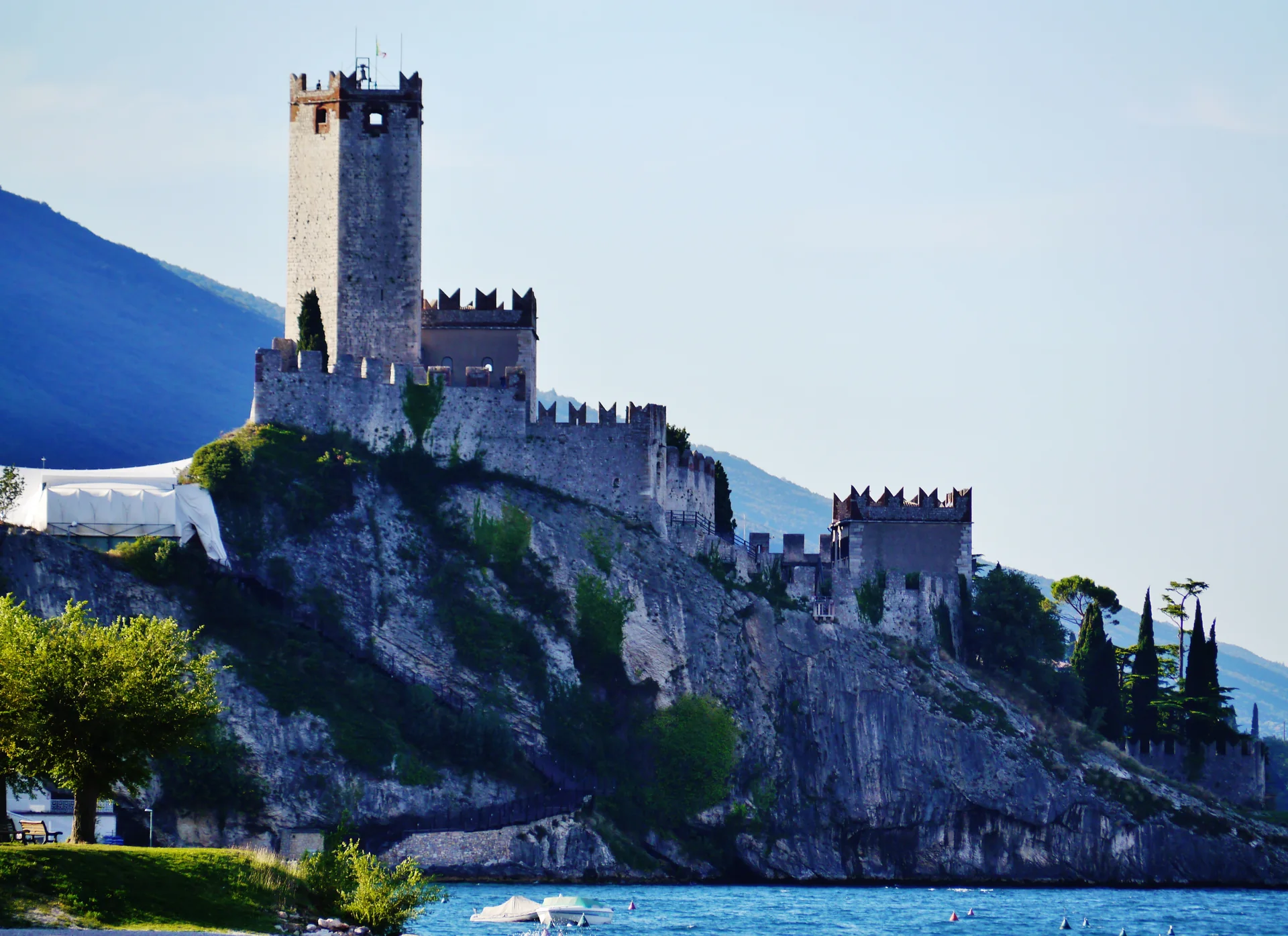 Castello Scaligero de Malcesine visto em luz natural, com torres de pedra, telhados da cidade e vegetação ao redor.