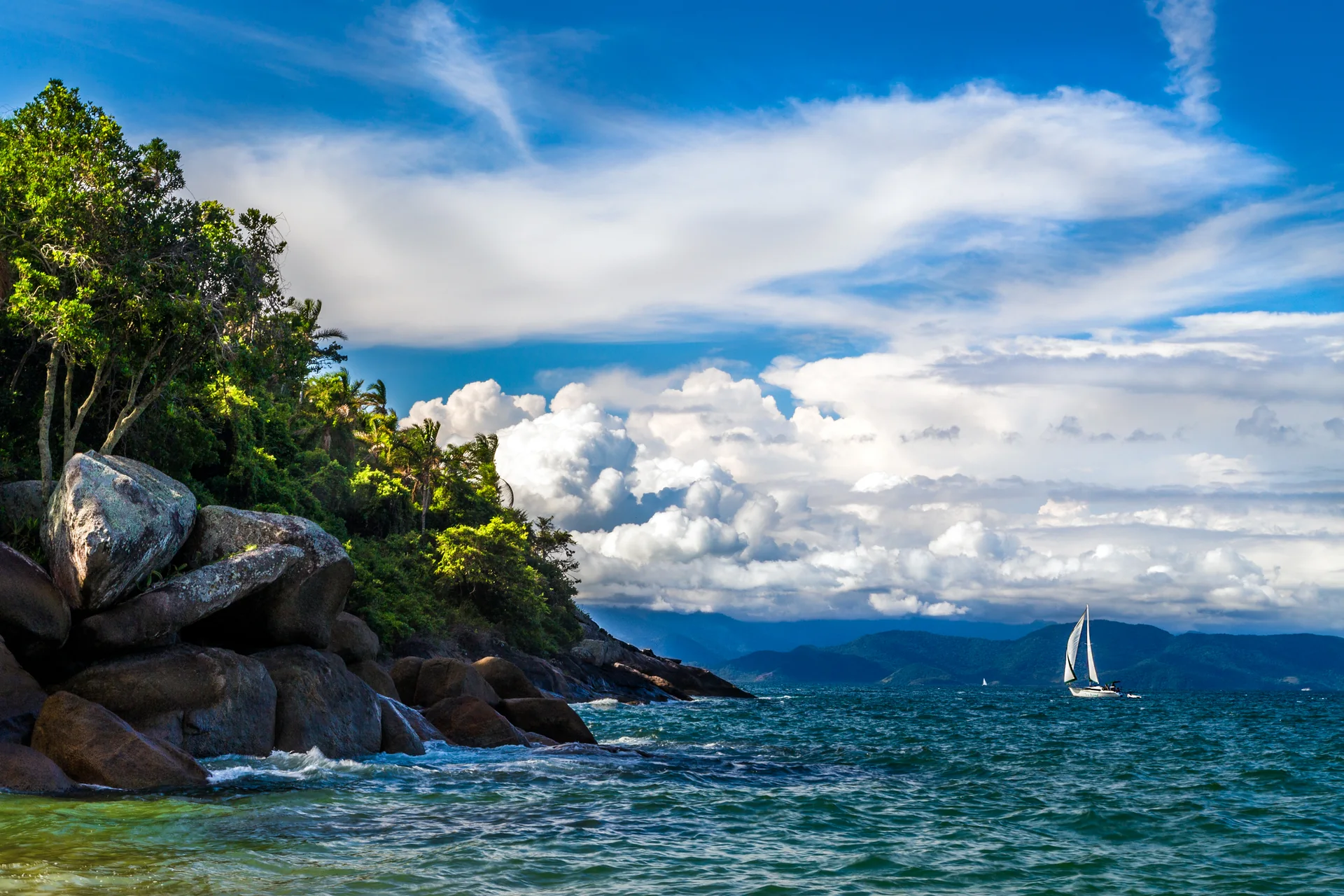Embarcação de grande porte navega no mar de Ilhabela diante de nuvens claras, vista da Praia da Feiticeira.