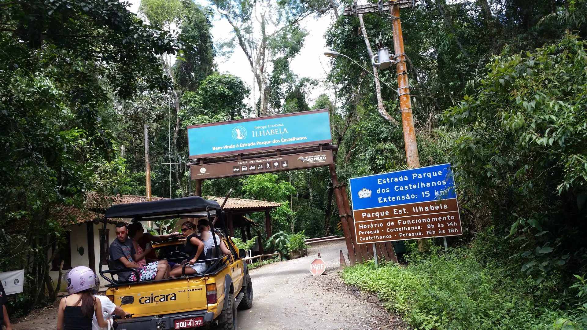 Veículo de passeio junto à guarita e às placas da entrada do Parque Estadual de Ilhabela, cercado por Mata Atlântica.