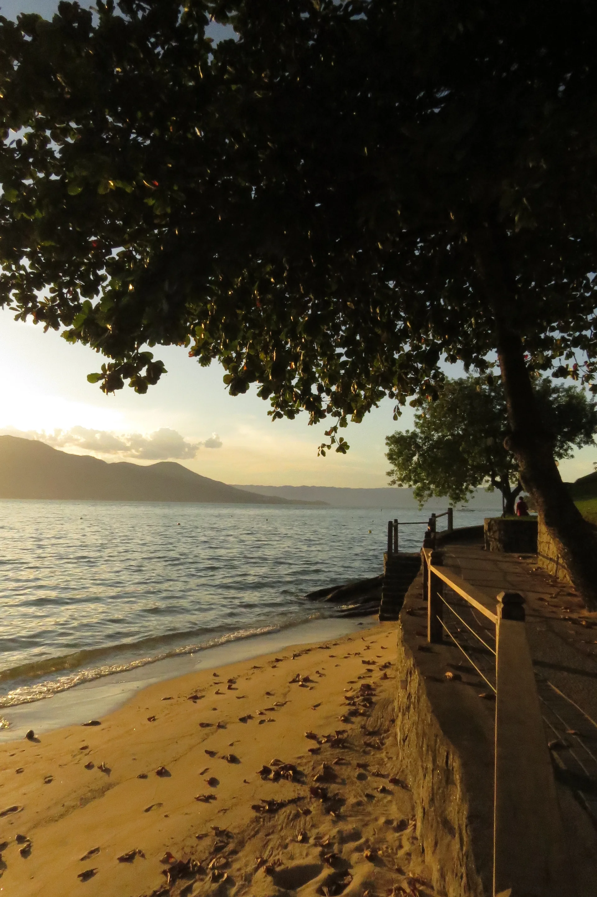 Ciclovia da Praia do Perequê em Ilhabela ao fim da tarde, ladeada por vegetação e pelo mar.