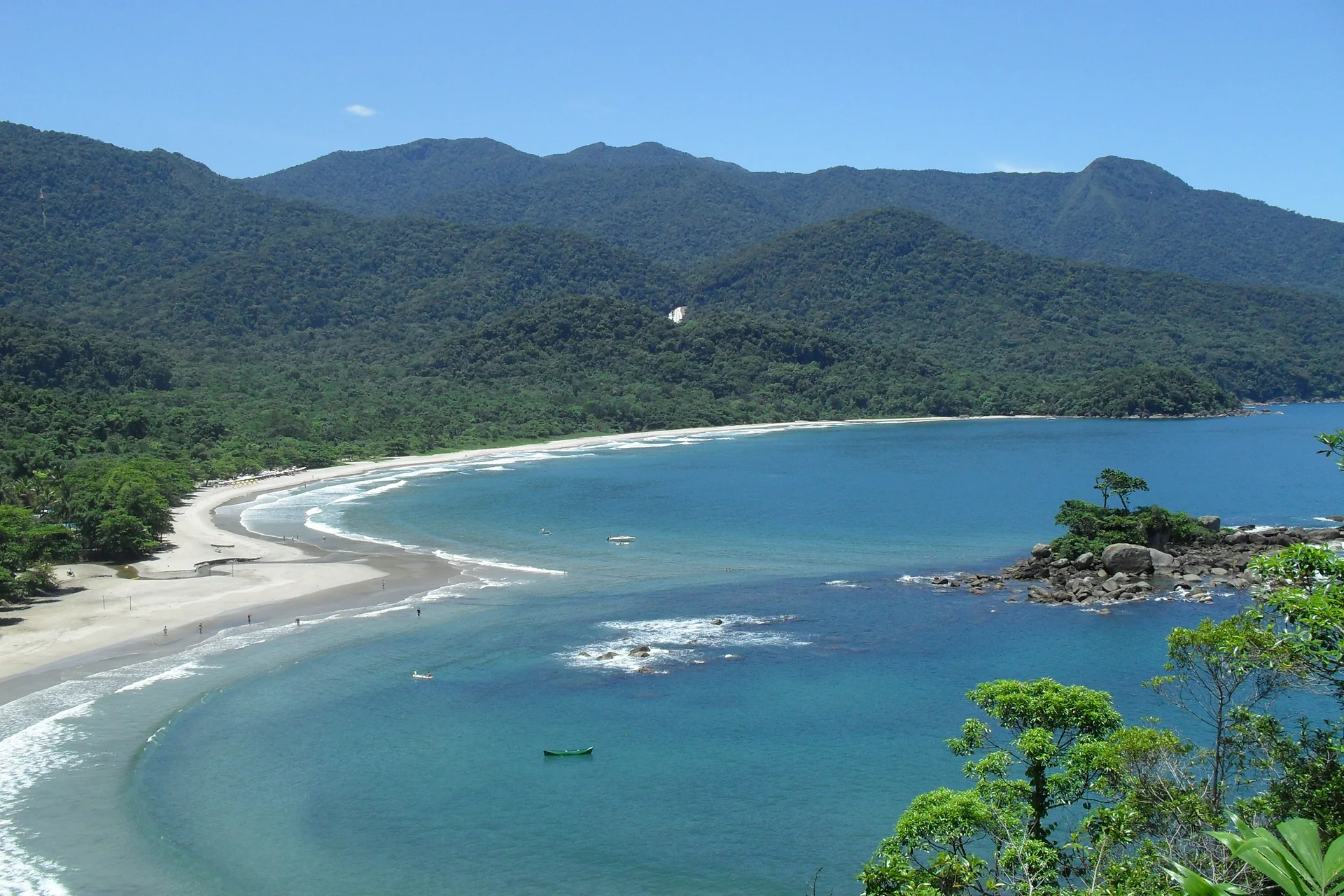 Baía da Praia dos Castelhanos em Ilhabela, com mar azul, faixa de areia clara e montanhas cobertas por Mata Atlântica.