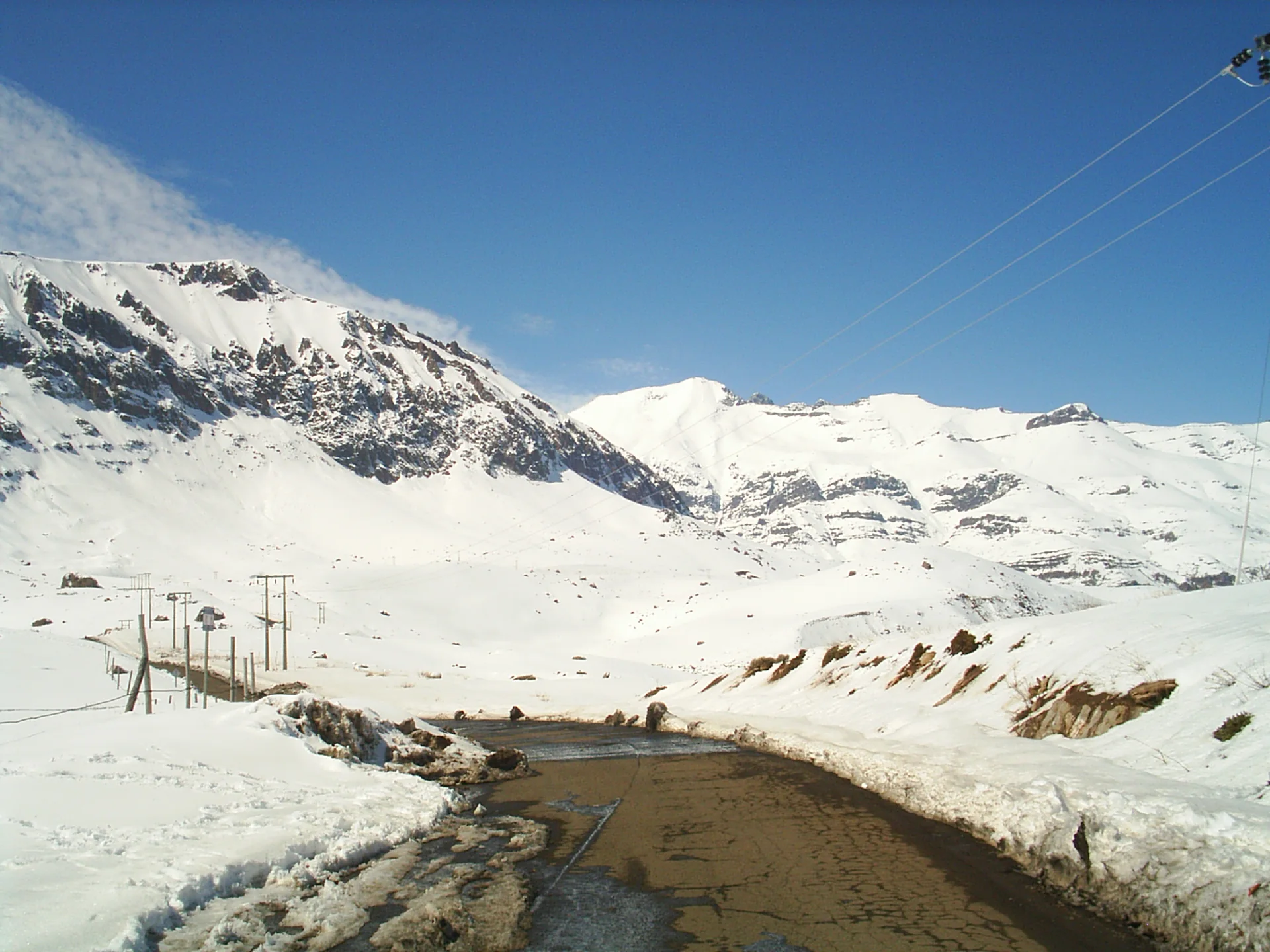 Montanhas cobertas de neve em Valle Nevado sob luz natural, com relevo exposto e céu azul.